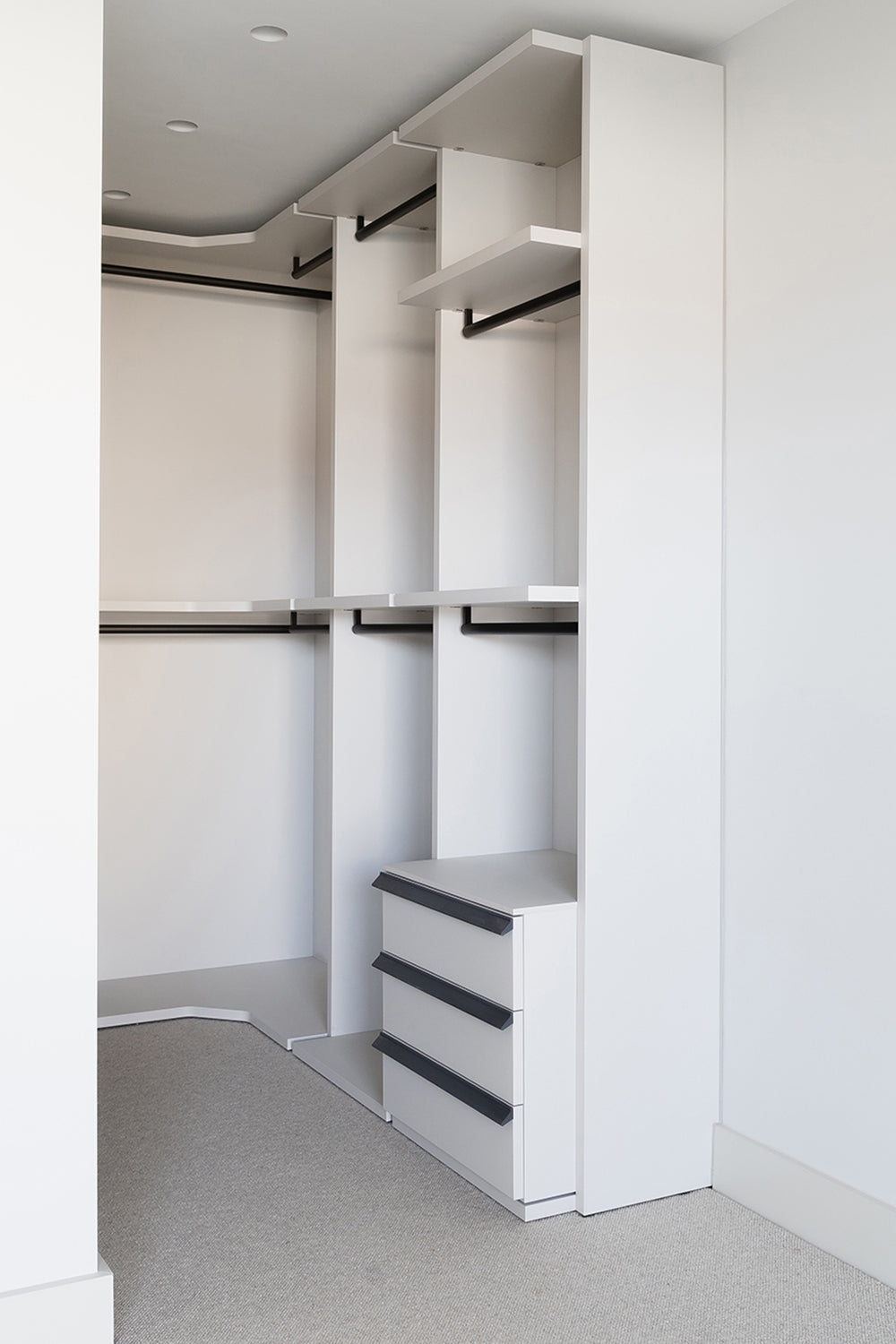 Contemporary built-in walk-in wardrobe with open shelving, hanging rails, and integrated drawers in a minimalist white finish with black accents.
