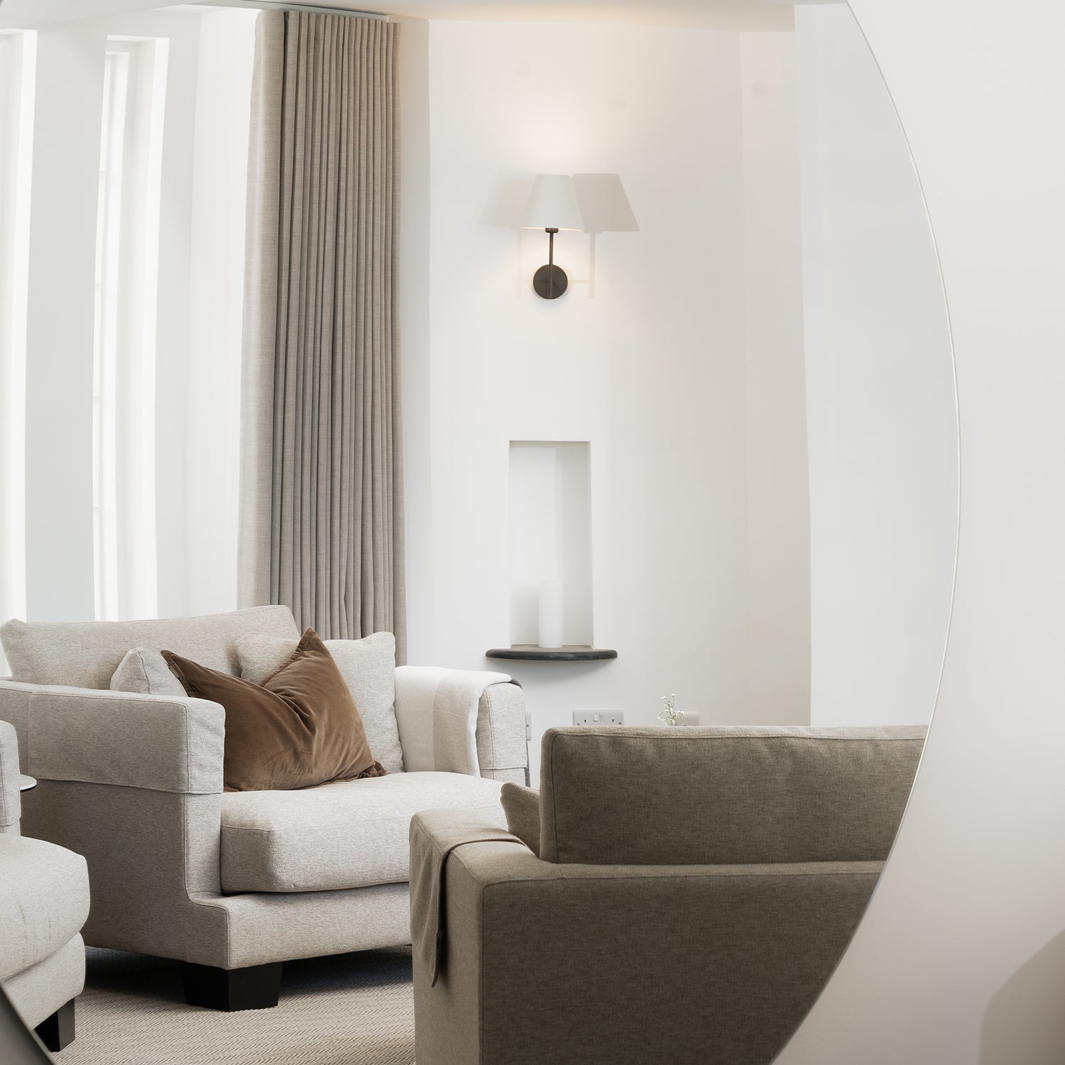 Elegant neutral-toned living room with plush armchairs, linen curtains, bronze wall sconce, and contemporary side table – luxury interior design with modern furniture for sophisticated home styling.