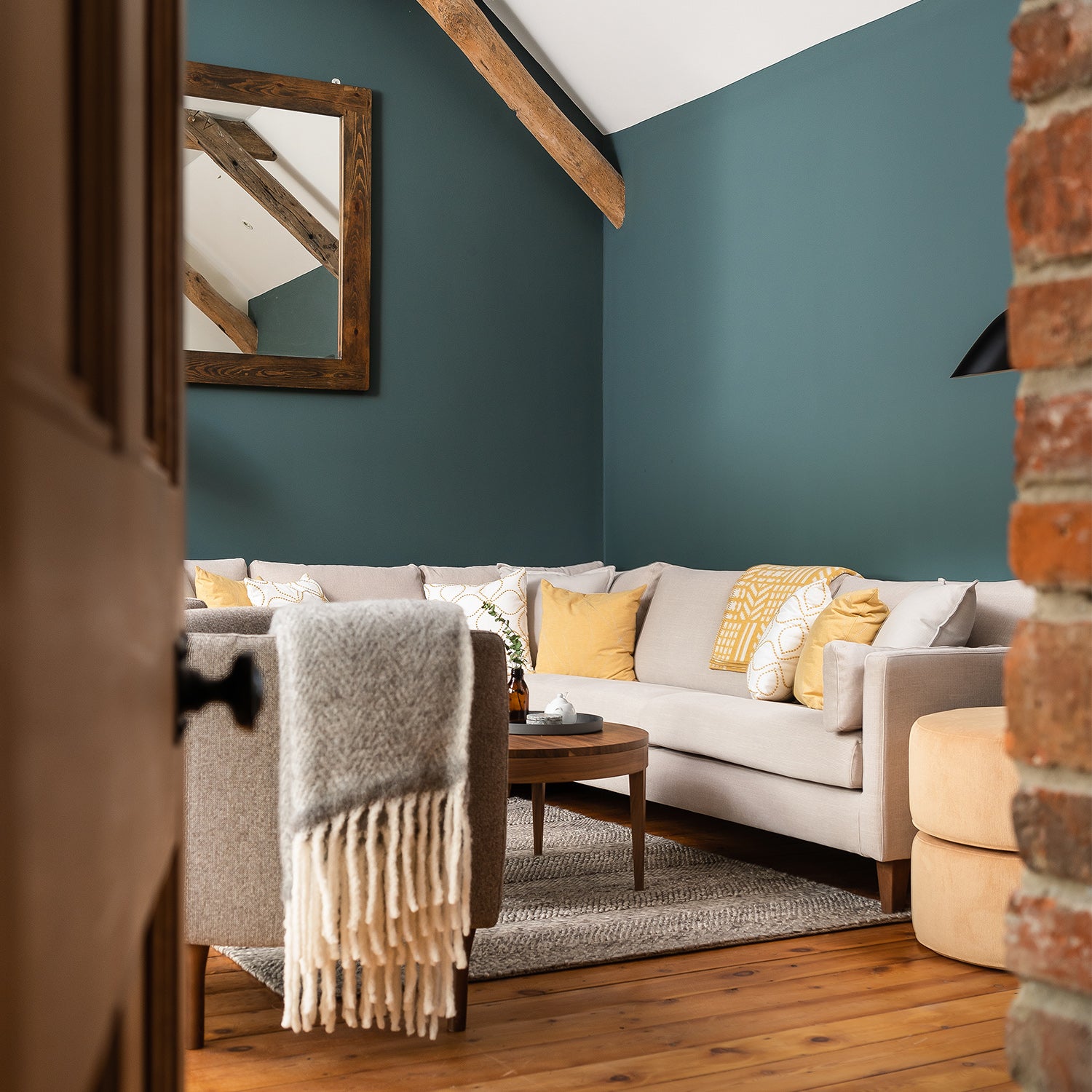 Inviting living room with deep teal feature wall, neutral corner sofa, mustard yellow accent cushions, rustic wood beams, and soft layered textiles – cozy modern farmhouse interior design with warm tones and natural textures.