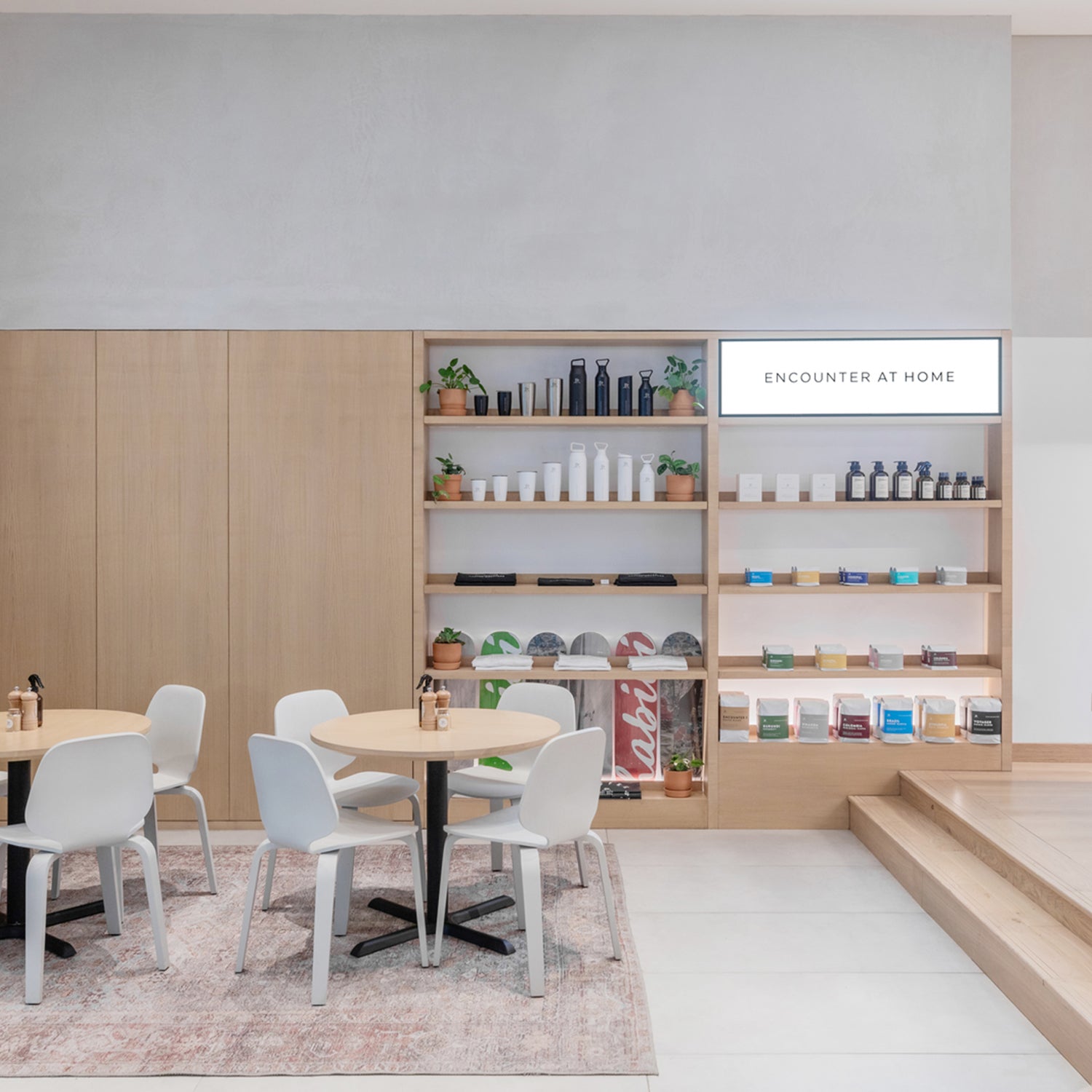 Contemporary commercial interior with minimalist café seating, oak shelving display, light wood finishes, and soft neutral palette – bespoke contract furniture and interior design services for retail and hospitality spaces in Cornwall.