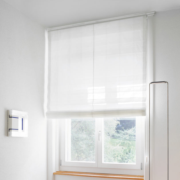 Elegant white Roman blind by Iroka Interiors, softly diffusing natural light in a modern Cornish home—perfect for stylish privacy and serene interiors.