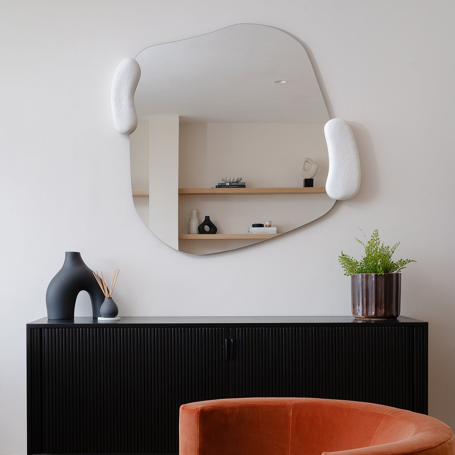 Modern living room interior with sculptural mirror, black fluted sideboard, ceramic vases, indoor plant and burnt orange velvet accent chair – minimalist design at The Cliffs, Carbis Bay.
