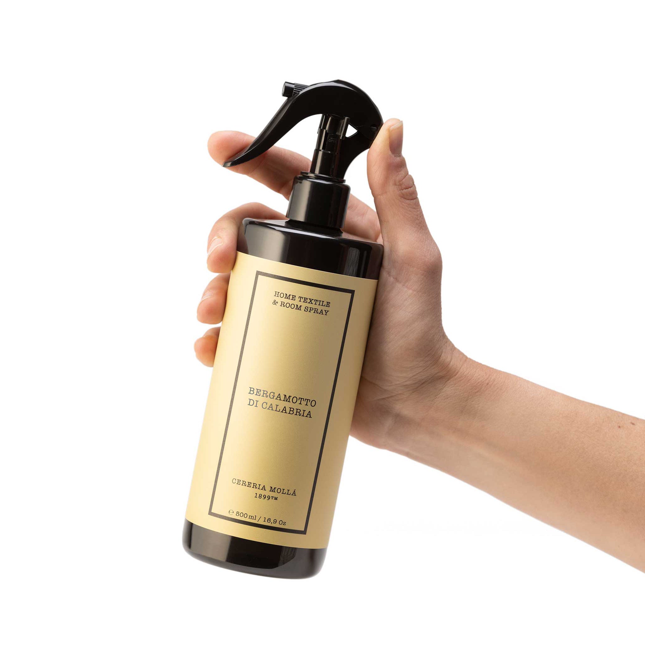 A hand holding a dark glass spray bottle with a beige label. The label reads 'Bergamotto di Calabria' and 'Cereria Molla'