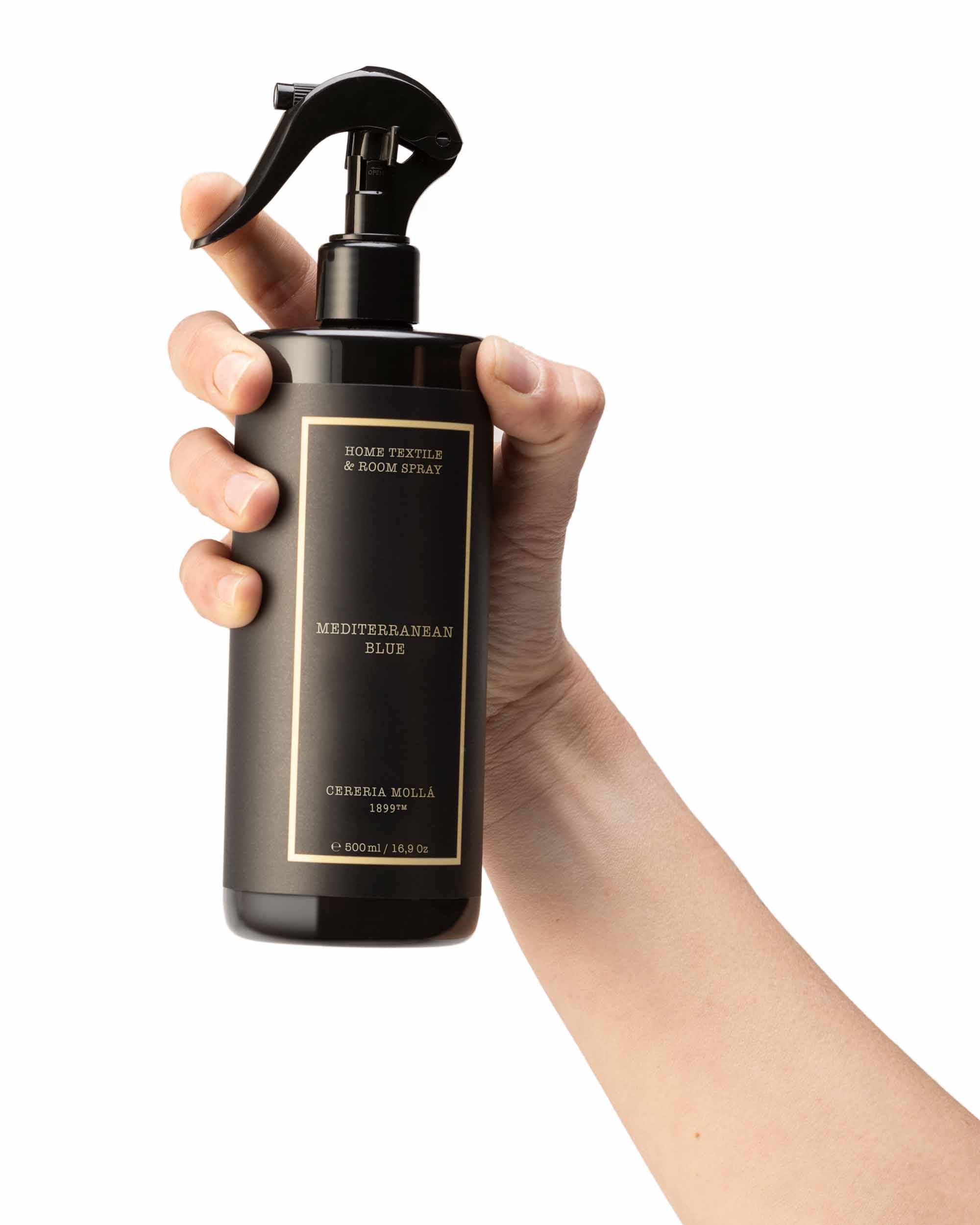 Hand holding a black spray bottle labelled 'Mediterranean blue' against a white background