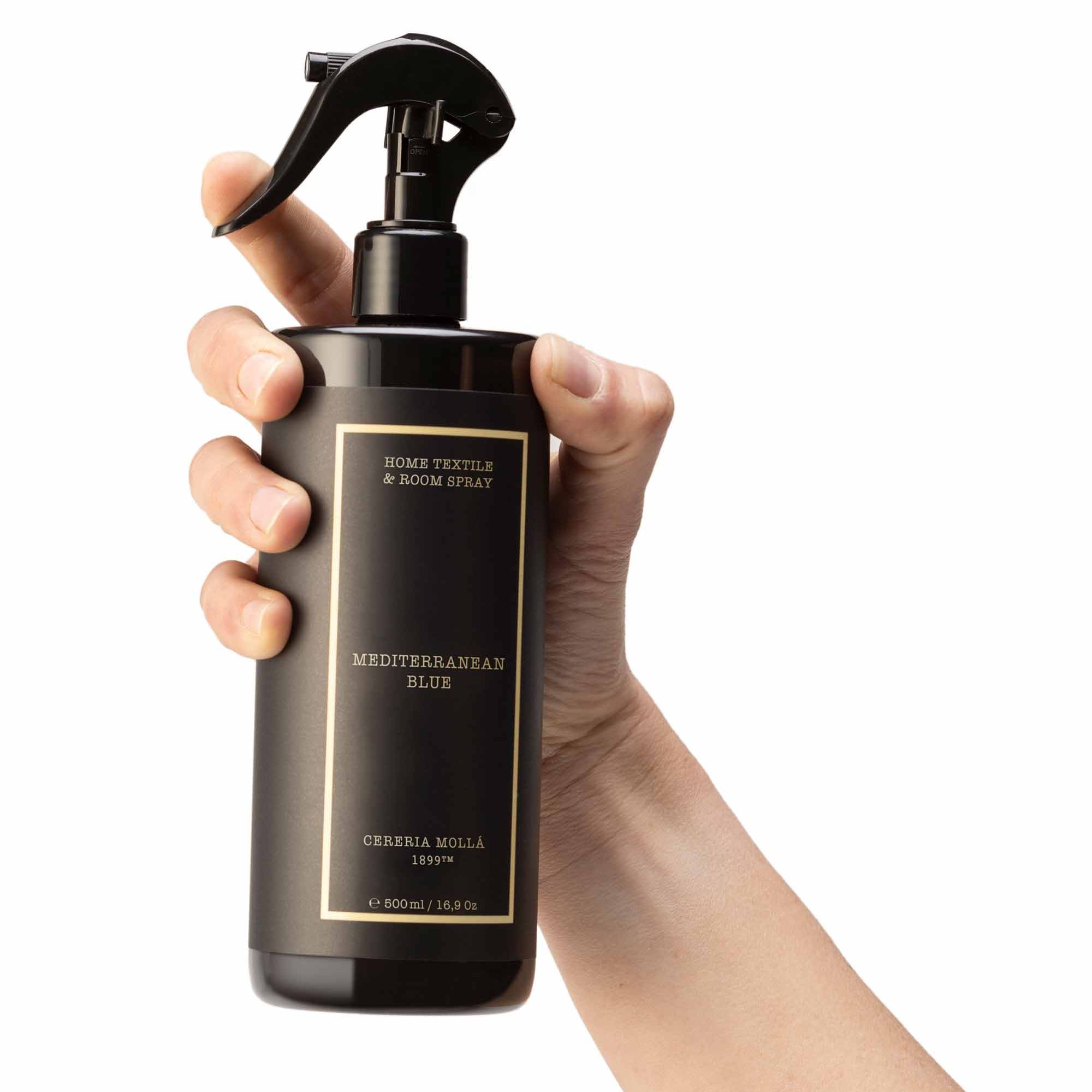 Hand holding a black spray bottle labelled 'Mediterranean blue' against a white background