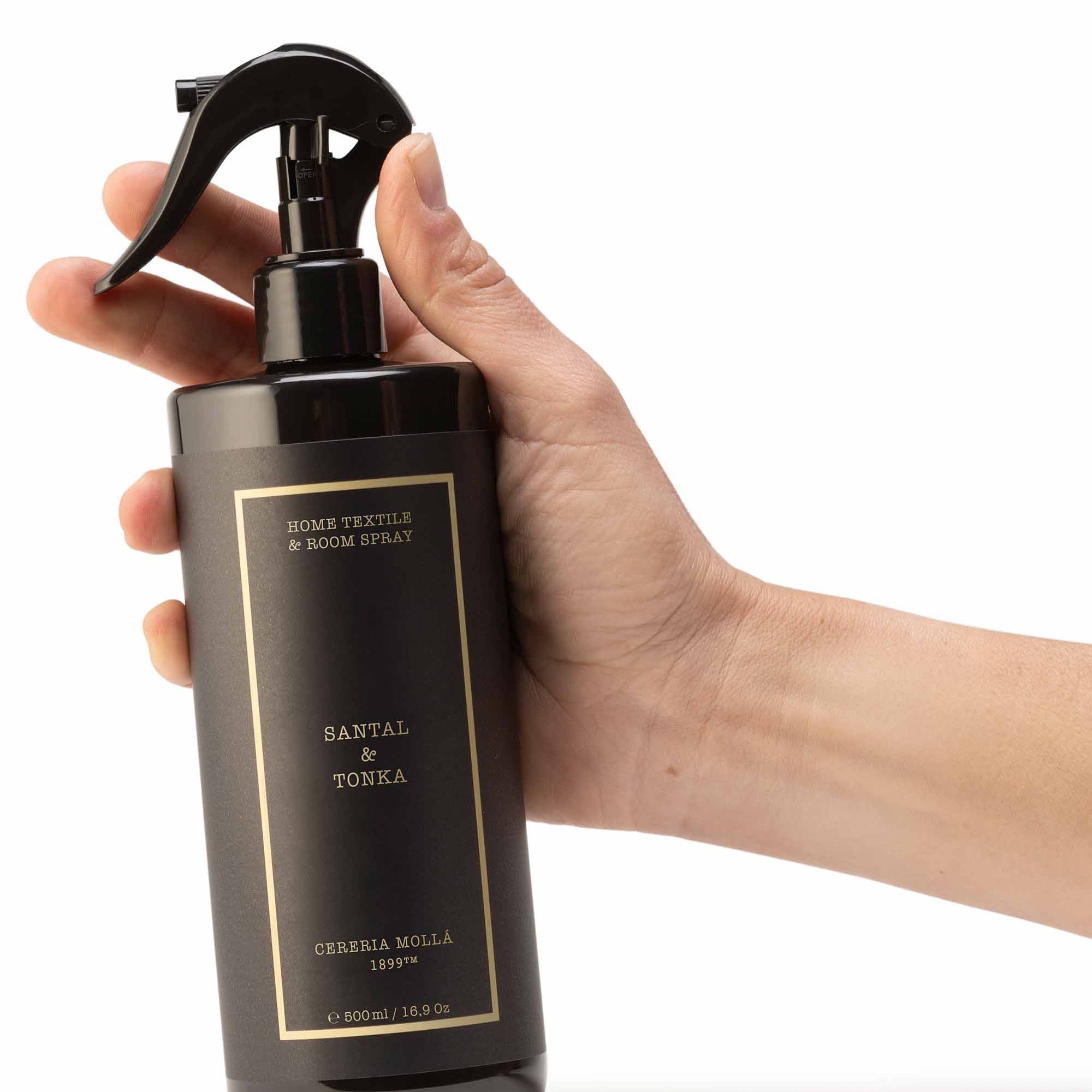Hand holding a black spray bottle labeled 'Santal & Tonka' against a white background