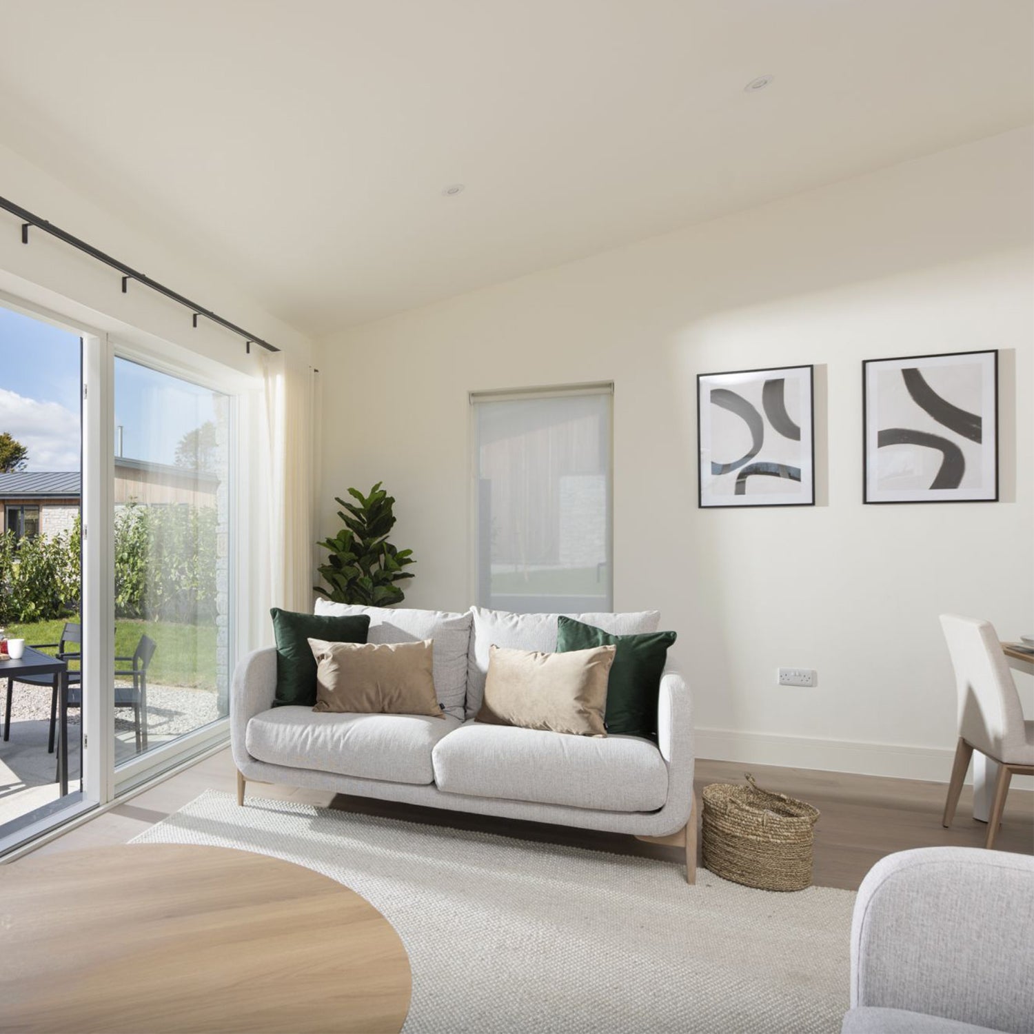 Bright modern living and dining space in Cornwall with white sofa, natural wood accents, abstract wall art, and sliding glass doors – minimalist interior design and contemporary furniture by Iroka Interiors.