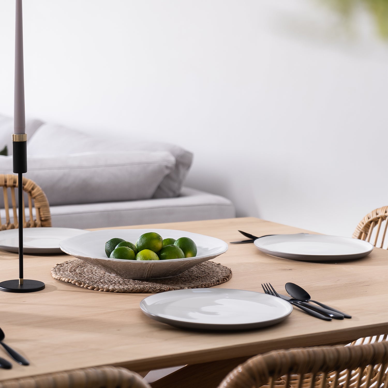 Contemporary dining setup at Iroka Interiors showroom in Cornwall featuring a natural wood table, minimalist black candlesticks, and woven rattan chairs — styled for a relaxed yet refined coastal home aesthetic.