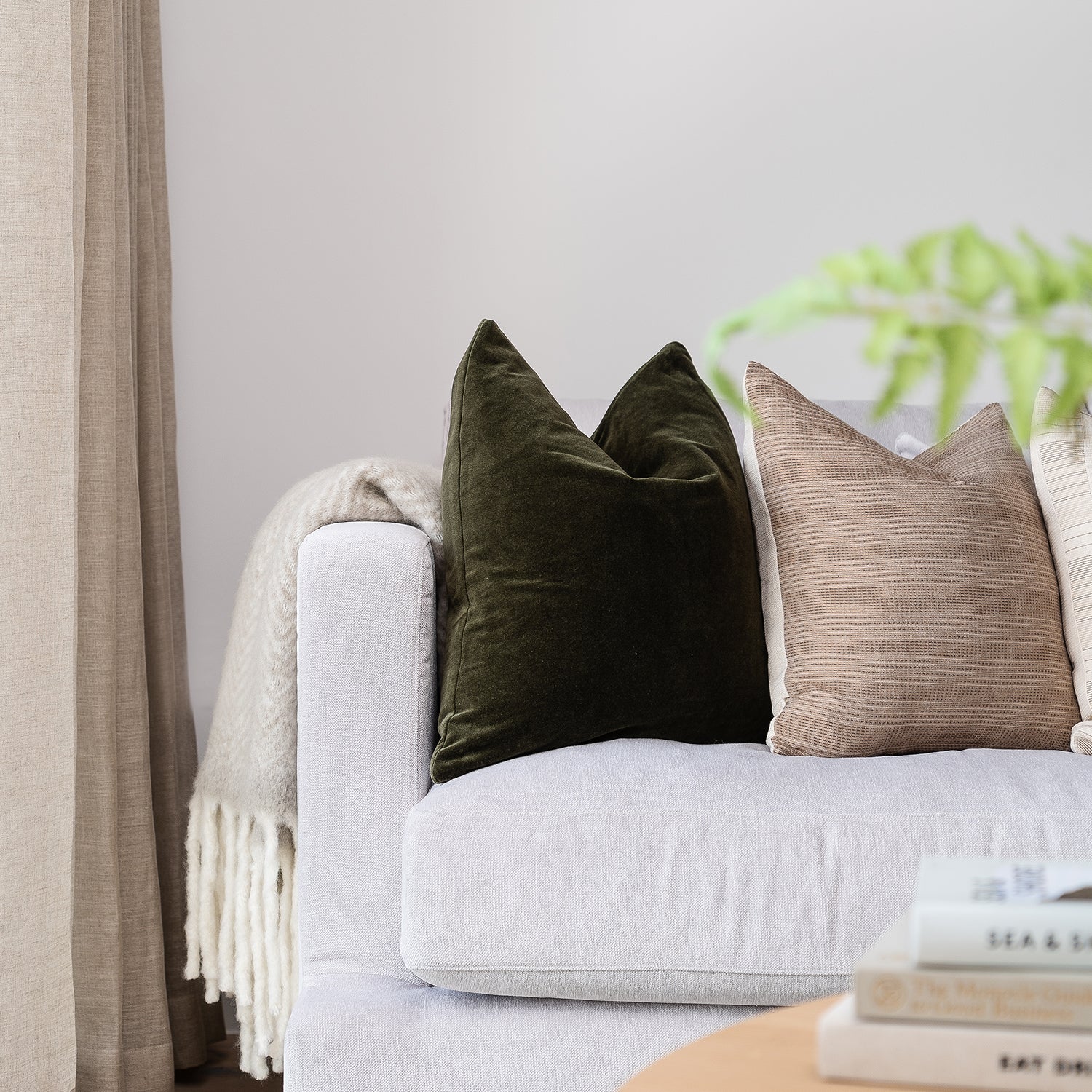 Detail of modern sofa styling in Cornwall showroom featuring white textured upholstery, velvet and woven scatter cushions, and soft neutral curtains – bespoke furniture and interior design services by Cornwall-based experts.