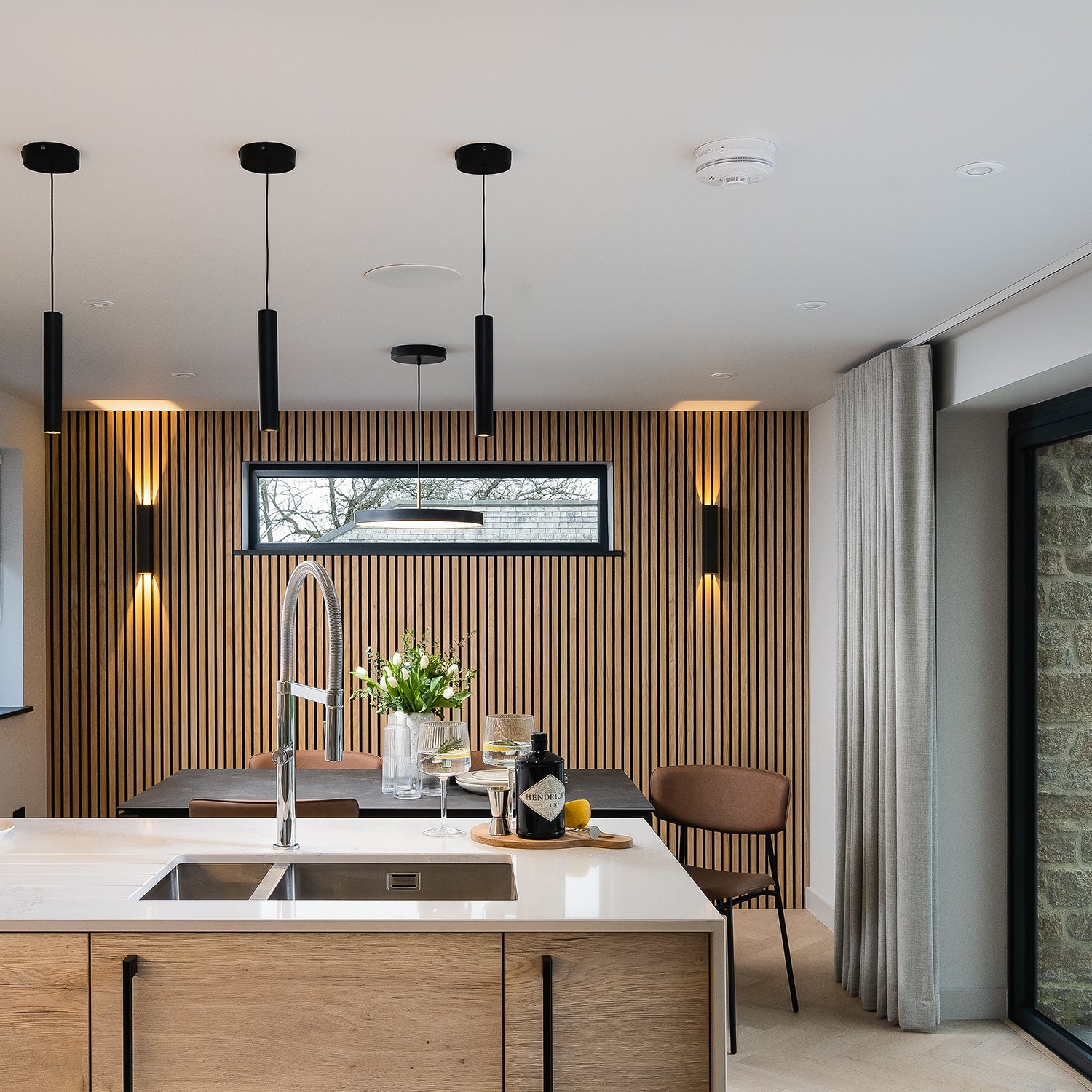 Contemporary kitchen with minimalist chrome pull-out tap, white quartz worktop, oak cabinetry, and fluted wood wall panel feature – bespoke kitchen design and installation by Iroka Interiors Cornwall.