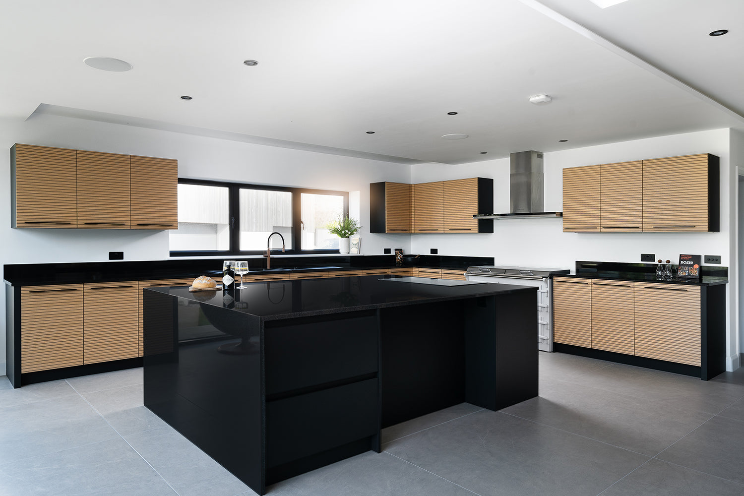 Modern bespoke kitchen design featuring matte black quartz island, horizontal slatted oak cabinetry, integrated appliances, and minimalist finishes – custom kitchen installation by Iroka Interiors in Cornwall.