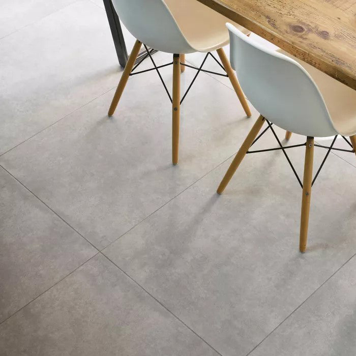 Modern dining area with Spacia Villa Concrete luxury vinyl tile flooring, featuring large-format grey stone-effect tiles, paired with white mid-century chairs and a rustic wooden table.