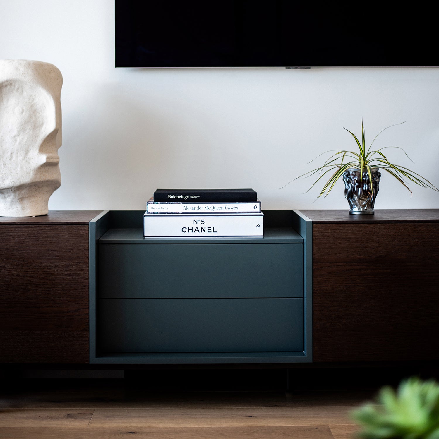Modern dark wood media console styled with sculptural decor, a minimalist black tray holding books, and a small potted plant beneath a wall-mounted TV.