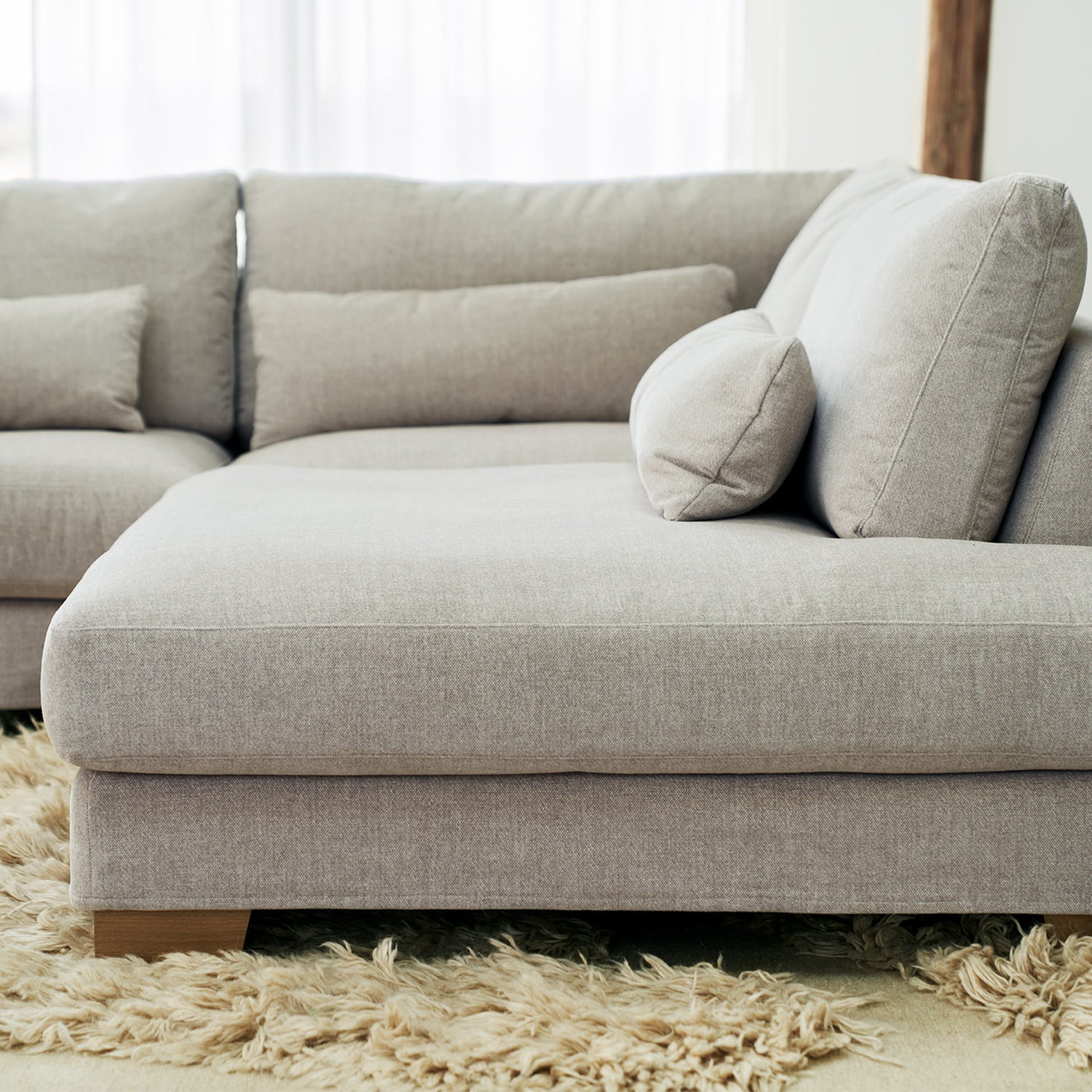 Modern modular sofa in soft grey fabric with deep chaise lounge and plush cushions, styled on a textured shaggy rug – contemporary living room seating for cozy minimalist interiors.