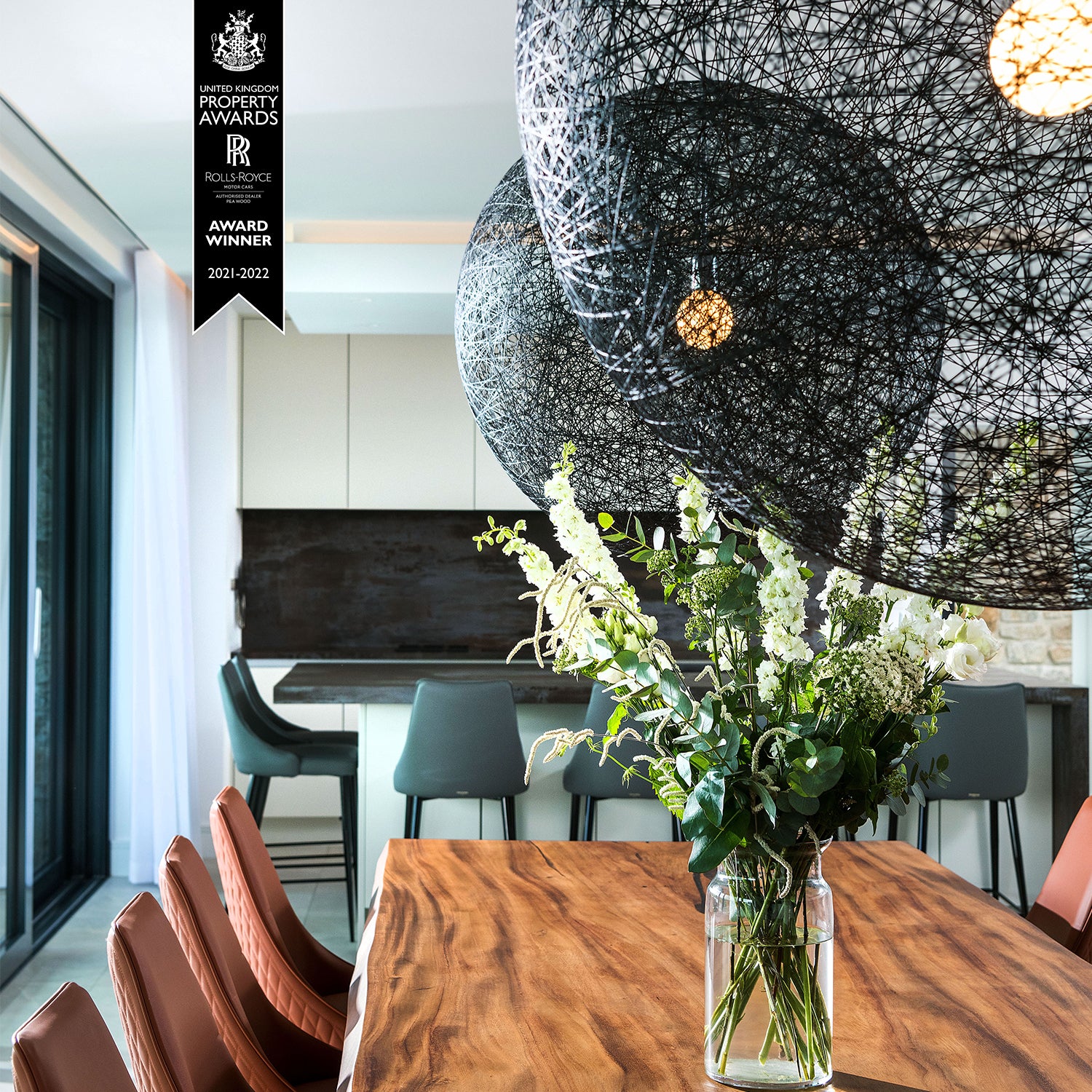 Luxury dining and kitchen space in Cornwall with live-edge wood dining table, leather dining chairs, bespoke mosaic wall feature, and statement lighting – high-end interior design and artisan furniture by Cornwall-based specialists.