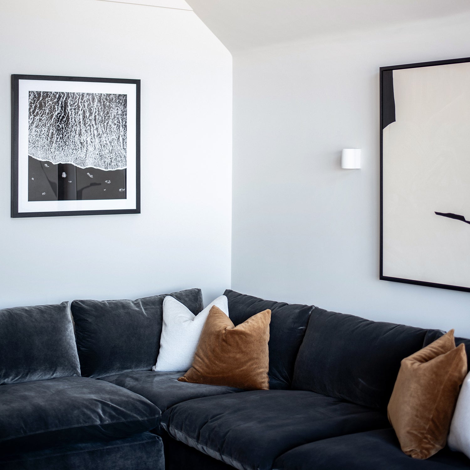 Contemporary living room at Pentire Townhouse, Newquay, featuring a dark grey sectional sofa, tan accent cushions, and monochrome abstract wall art.
