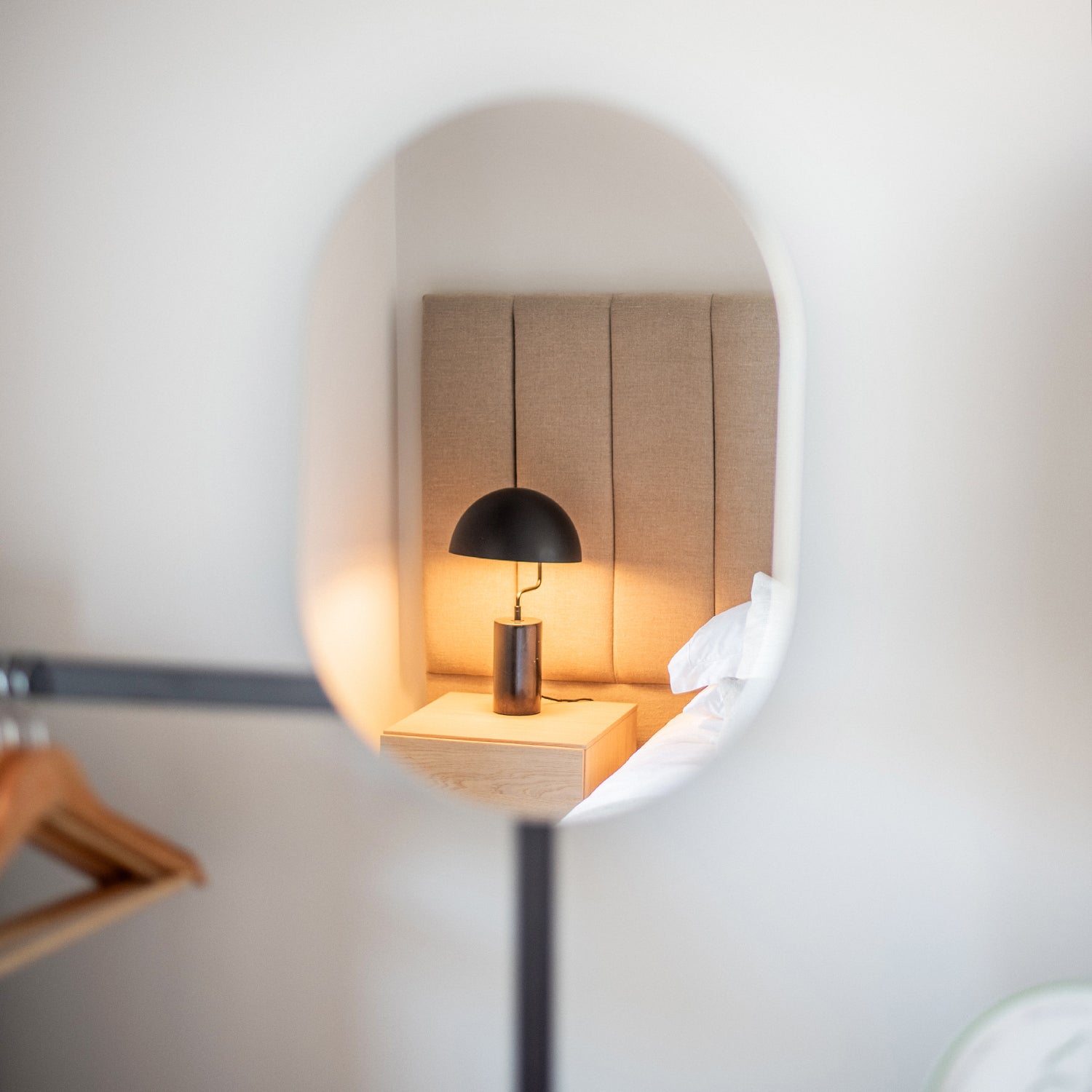 Modern alcove feature with built-in wood paneling and soft lighting, complemented by a sculptural black table lamp and minimalist clothes rail.
