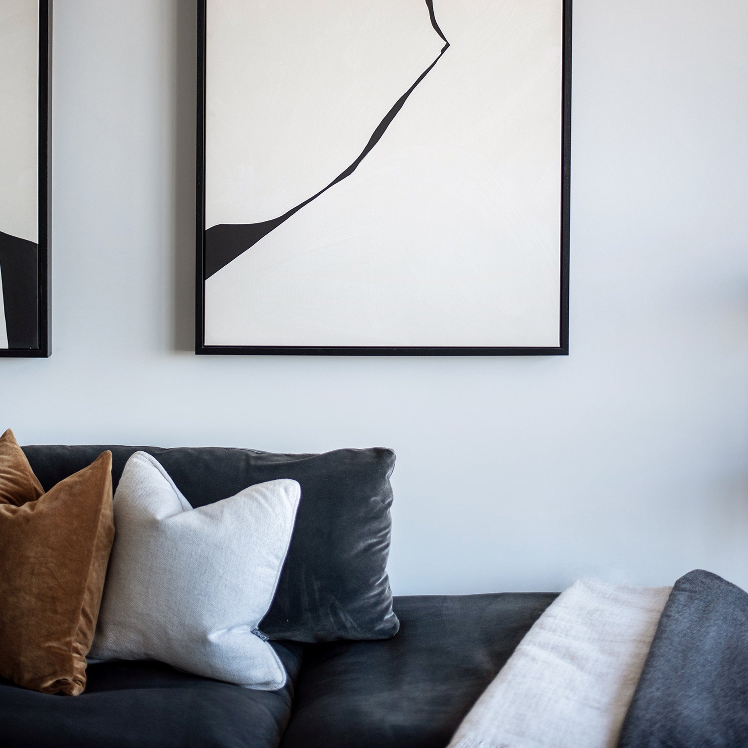 Contemporary lounge corner with a charcoal velvet sectional sofa, featuring neutral-toned scatter cushions and abstract black-and-white artwork framed above on a soft grey wall.