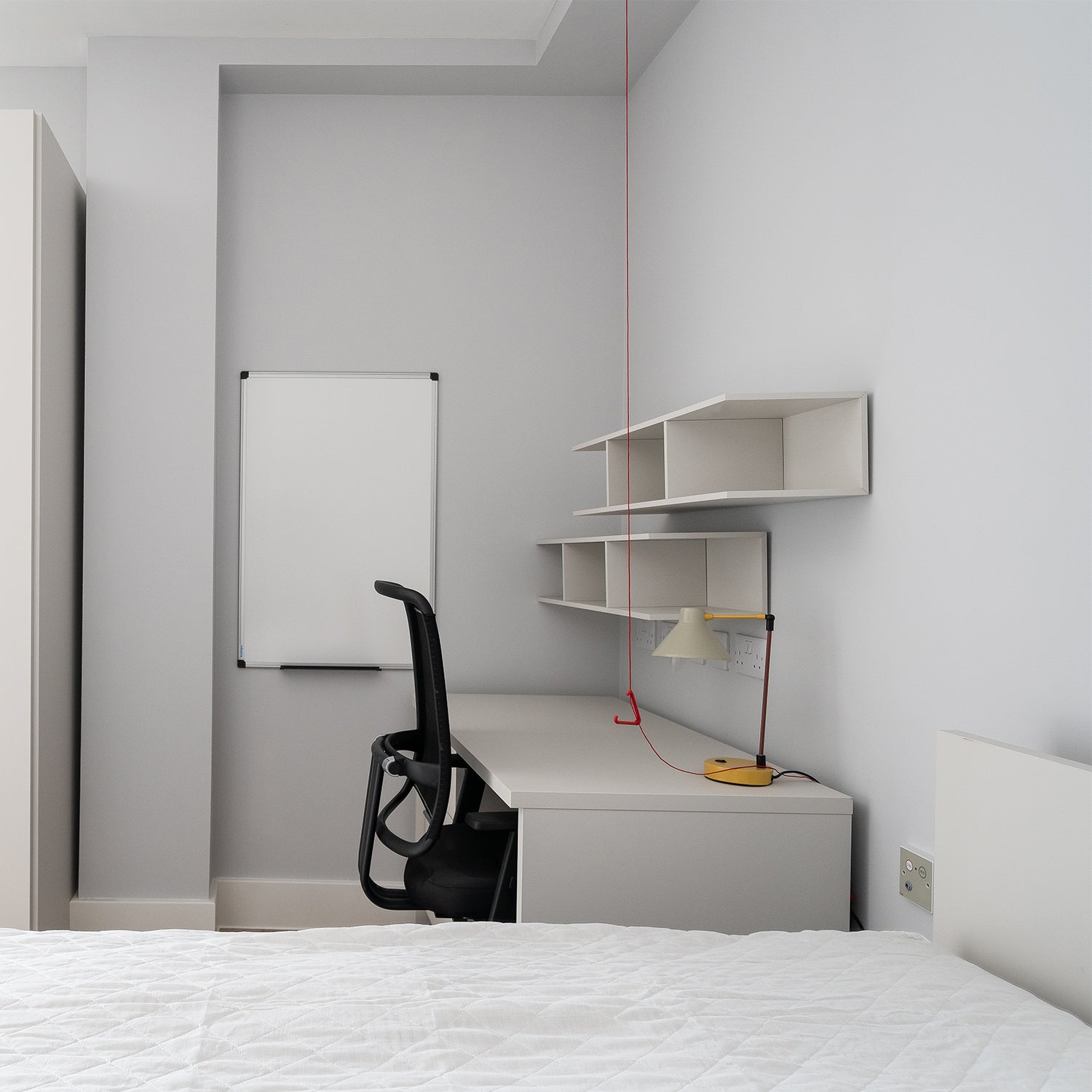 Minimalist student bedroom interior in Falmouth designed by Iroka Interiors, featuring a modern study desk with shelving, ergonomic office chair, wall-mounted whiteboard, and neutral decor to promote focus and comfort in university living spaces.