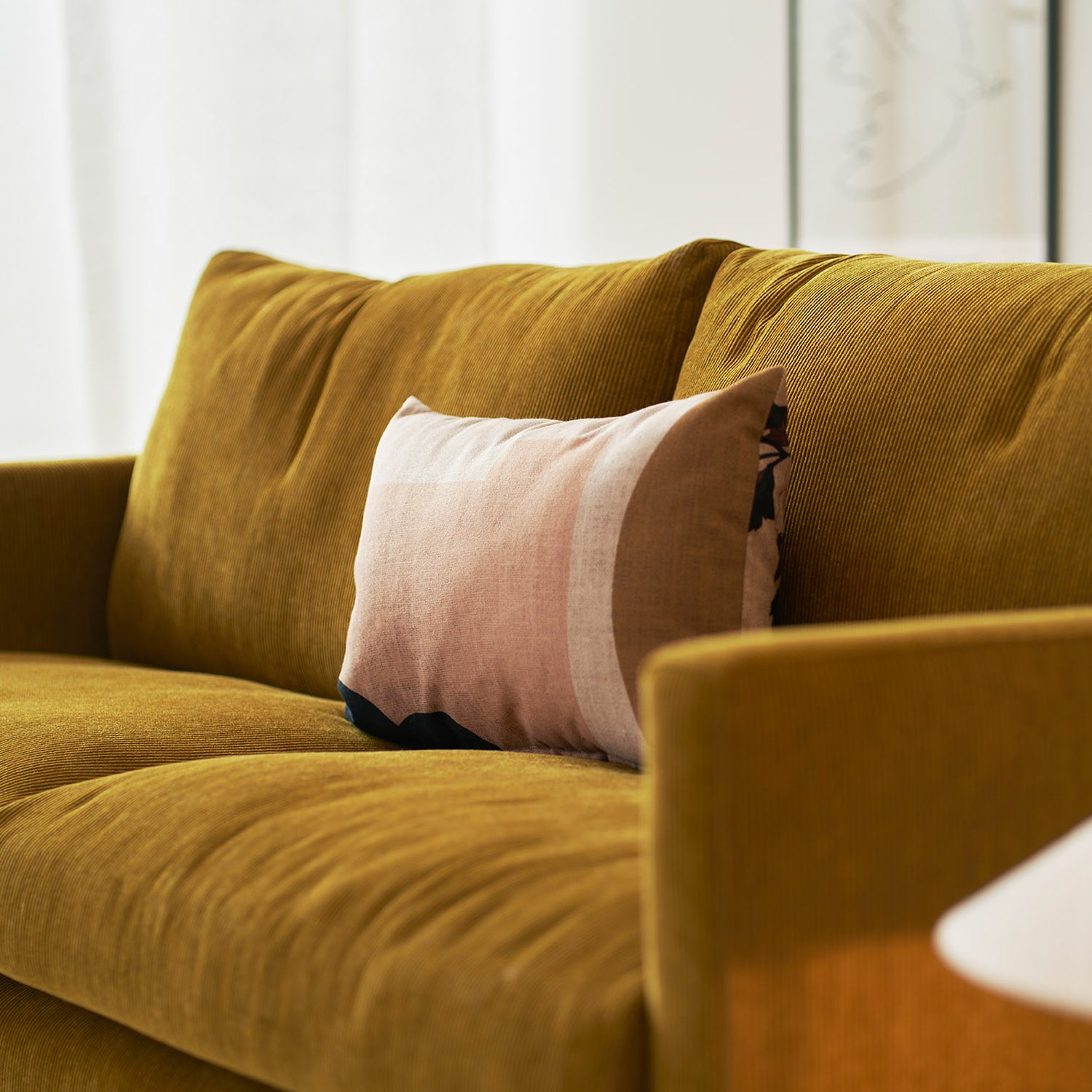 Detail of a mustard yellow corduroy sofa with tailored cushions and a muted pink patterned lumbar pillow, styled in soft natural light showcasing Mastrella’s tactile and design-forward upholstery.