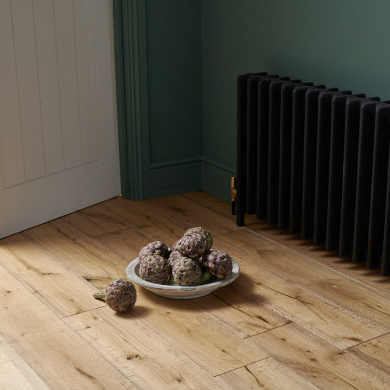 Berkeley Cottage engineered oak wood flooring in a light rustic finish, styled with a bowl of fresh artichokes and a bold black radiator against teal walls for a warm country-inspired interior