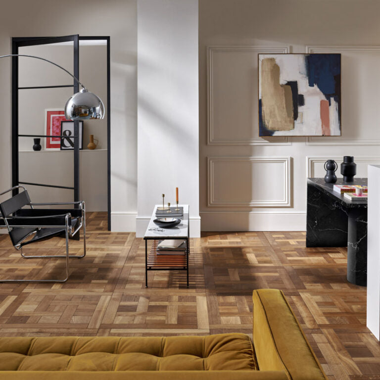 Clarence Aged Oak panel wood flooring in a modern living room with a rich geometric parquet design, paired with contemporary furniture, abstract wall art, and a mustard velvet sofa for a bold and elegant interior.