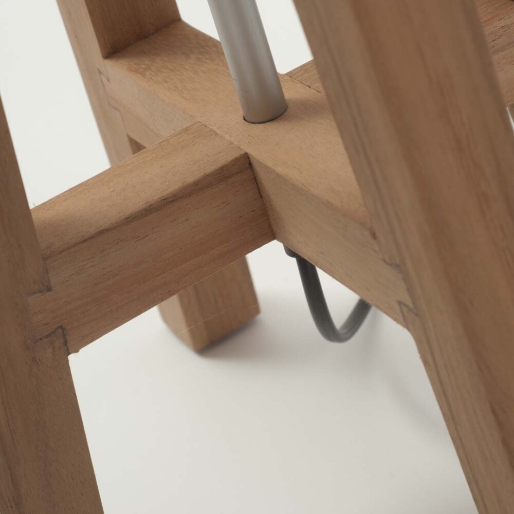 Close-up detail of a wooden lamp frame with a silver metal leg support and a black cable visible underneath on a white background.