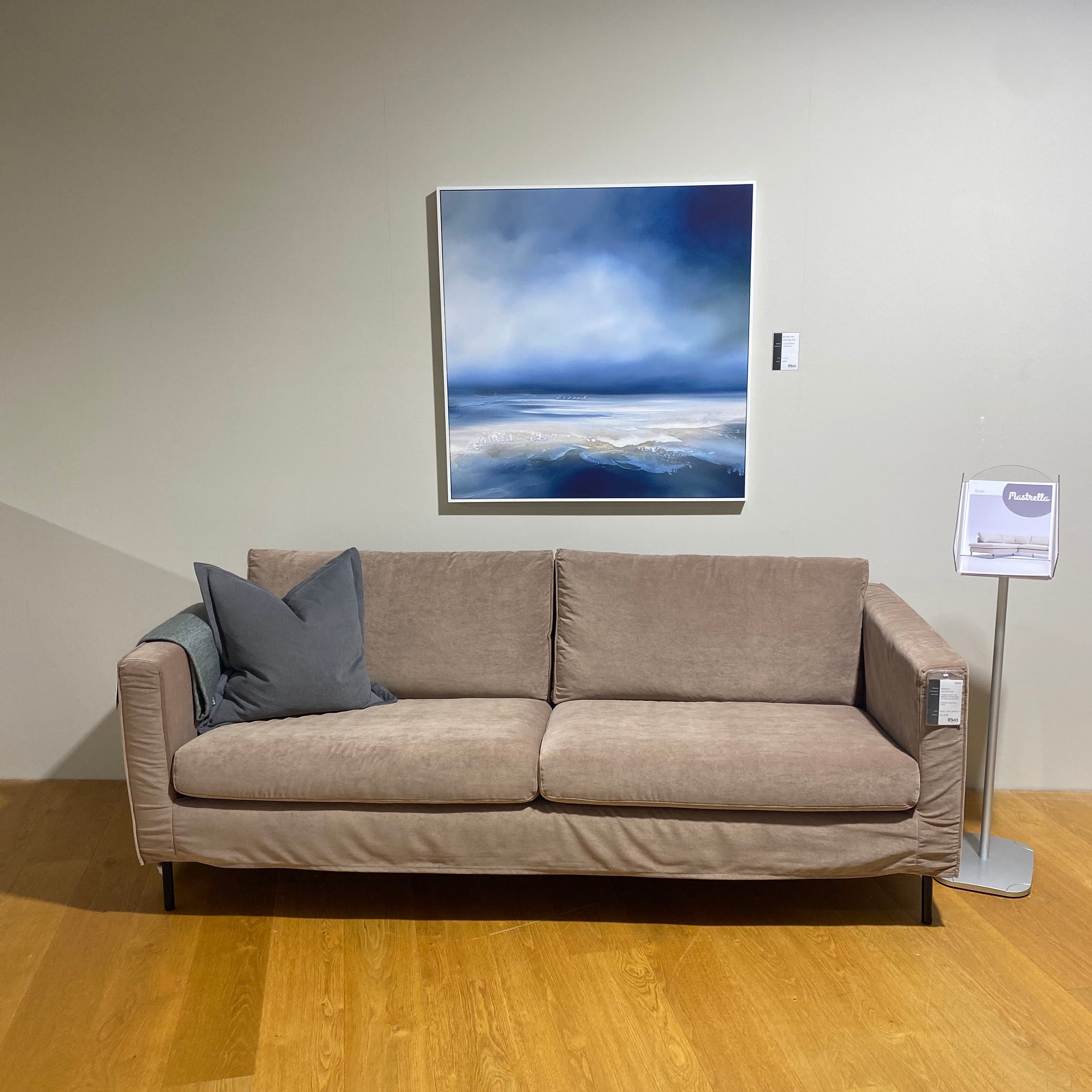 Beige sectional sofa with a gray pillow against a beige wall with a painting.