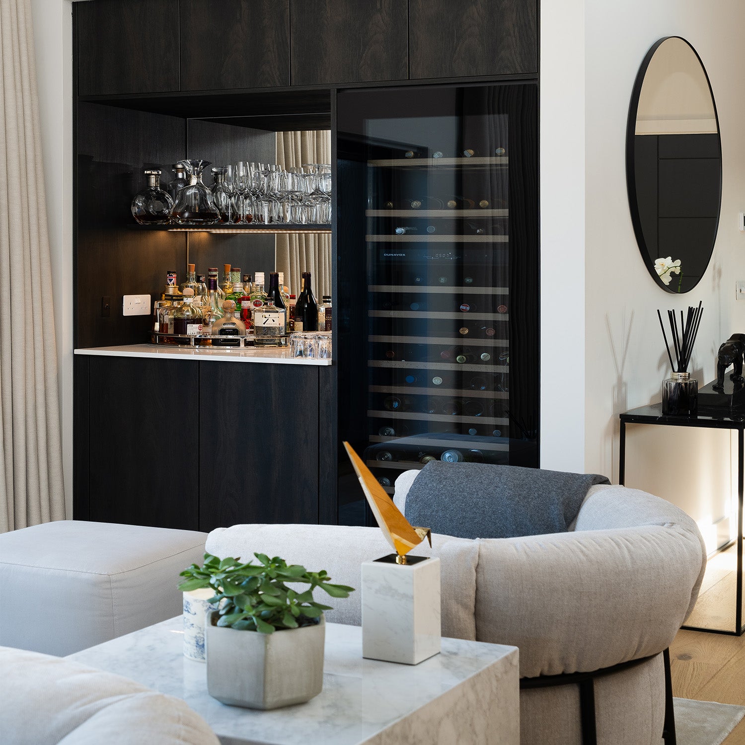 Stylish modern home bar with black cabinetry, built-in wine fridge, glassware display, and marble countertop in a luxury living room interior – ideal for contemporary home bar design inspiration.