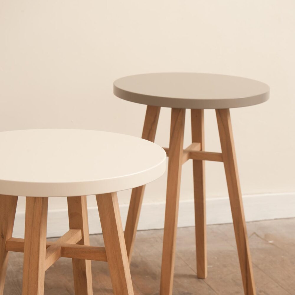 Two round nesting side tables with light natural wood legs and contrasting tabletops, one in white and one in light grey, set against a neutral cream wall.