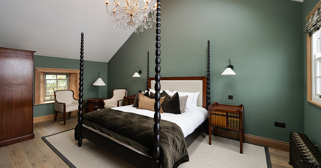 Transformed master bedroom with dark green feature wall, four-poster bed, luxury layered bedding, vintage wood nightstands, and mid-century modern accents – elegant bedroom makeover after renovation.