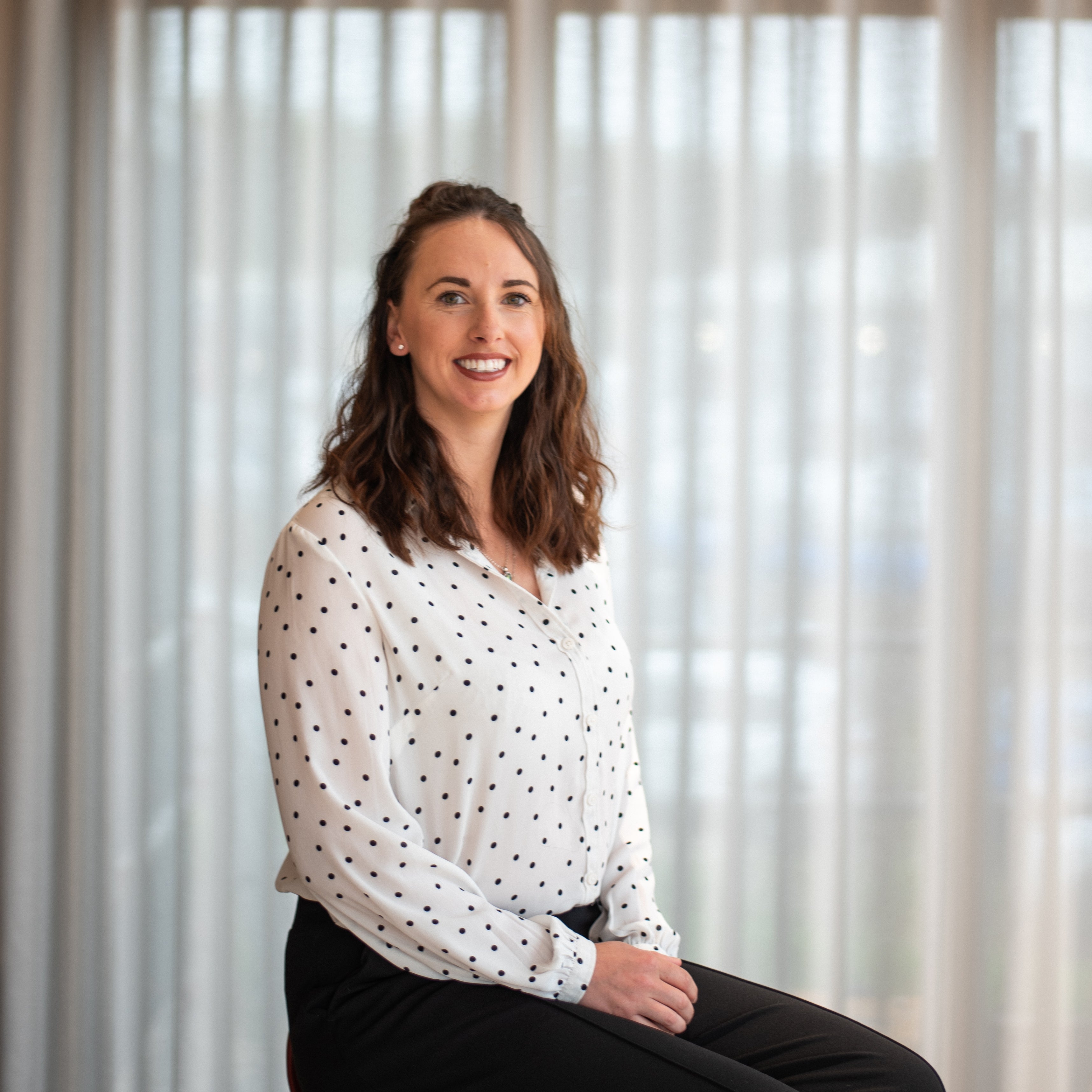 Milly, flooring manager at Iroka Interiors in Hayle, Cornwall – expert in premium flooring solutions, pictured smiling in front of sheer window dressings.