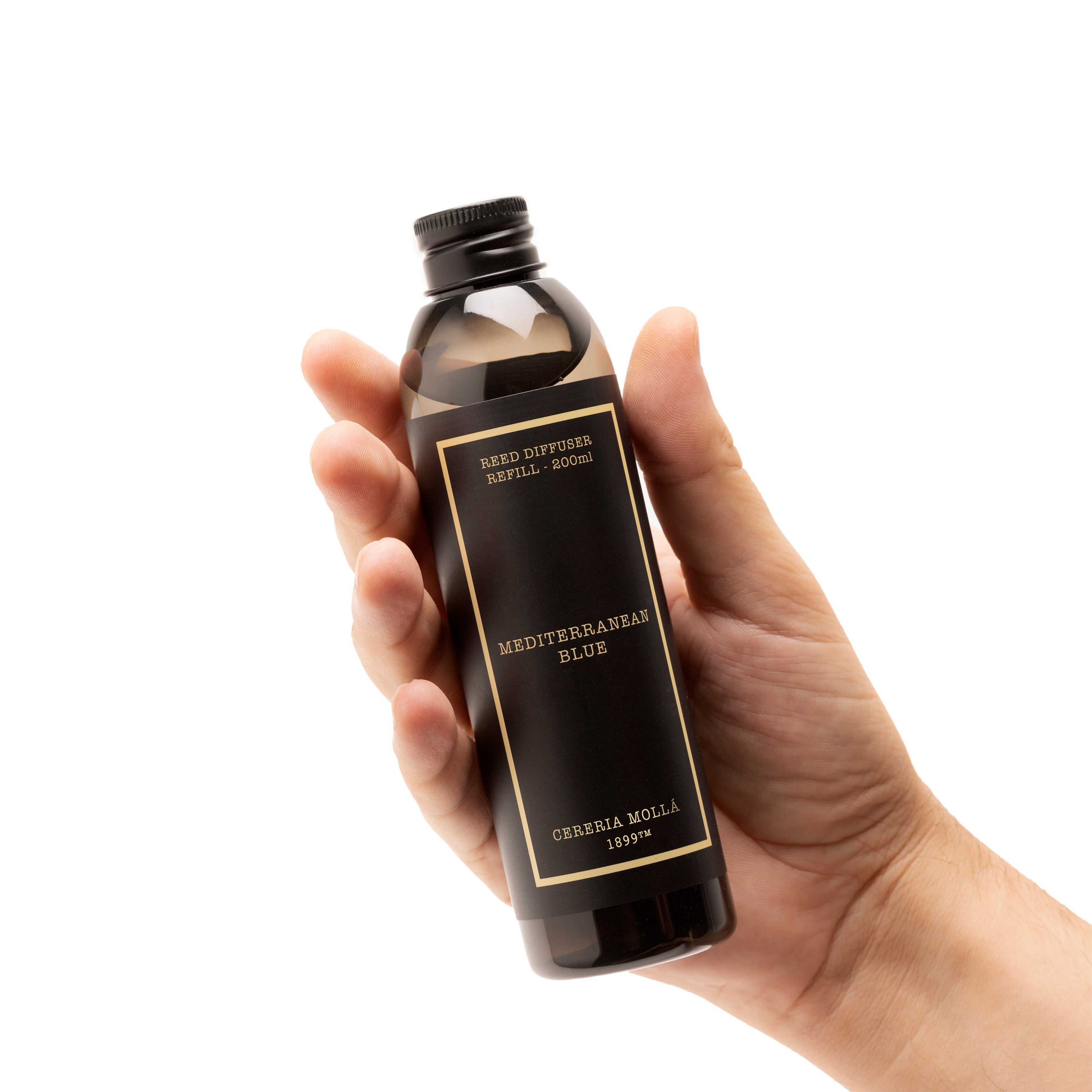 A hand holding a dark amber glass bottle of Cerreria Molla' Mediterranean Blue' essential oil against a solid white background.
