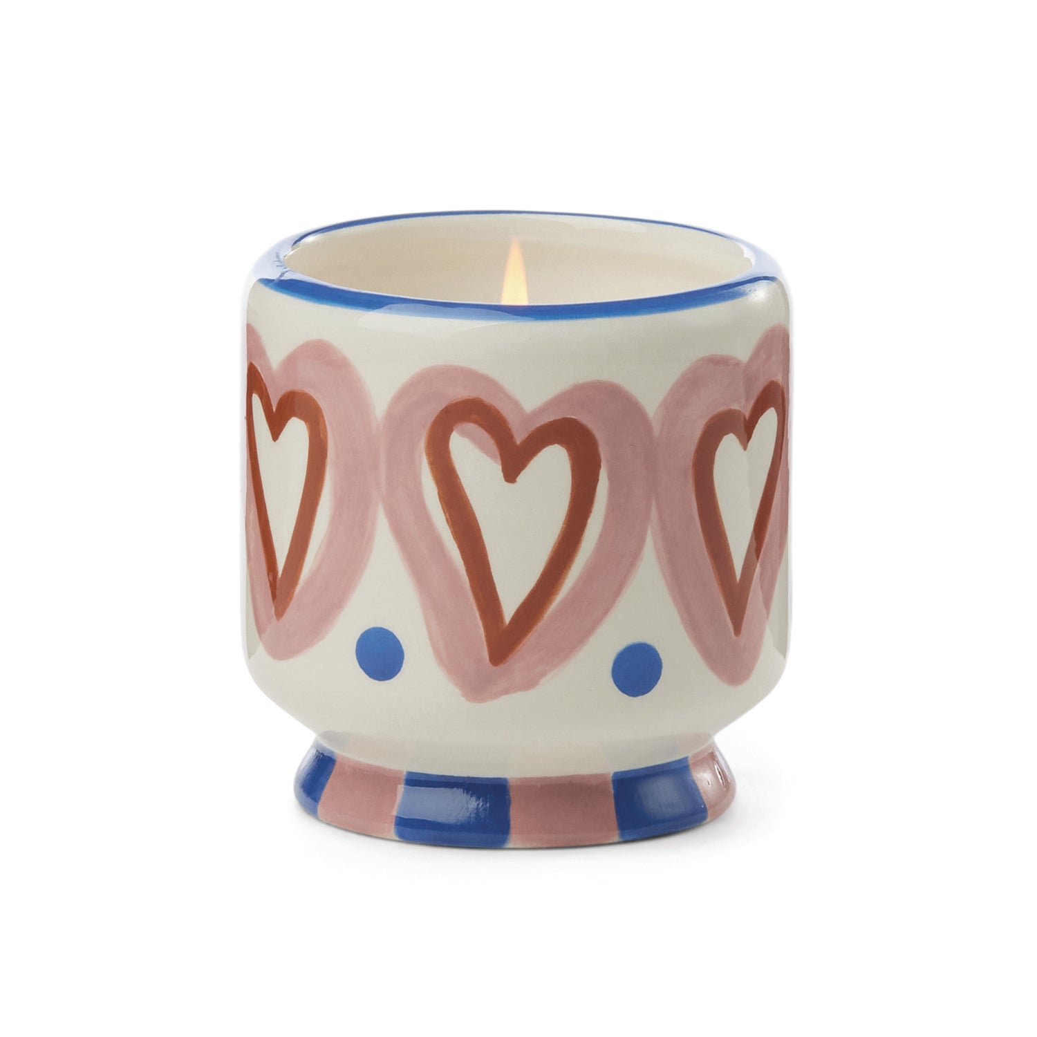 A small ceramic candle holder with a lit candle inside, decorated with pink hearts, red heart outlines, blue dots, and blue and pink striped detailing on a white background.