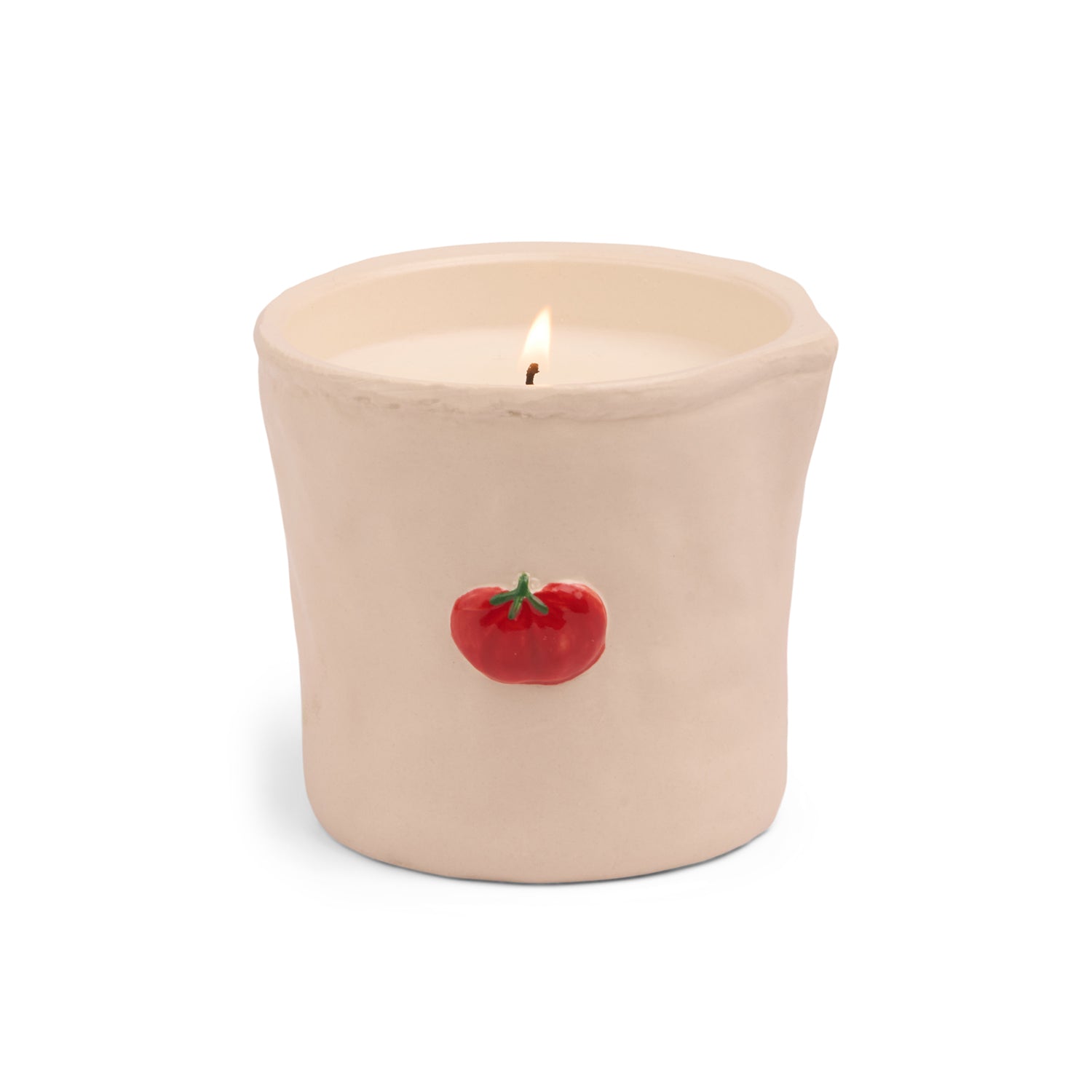 A lit cream-colored ceramic candle in a cylindrical pot with a small red tomato graphic on the front, set against a plain white background.