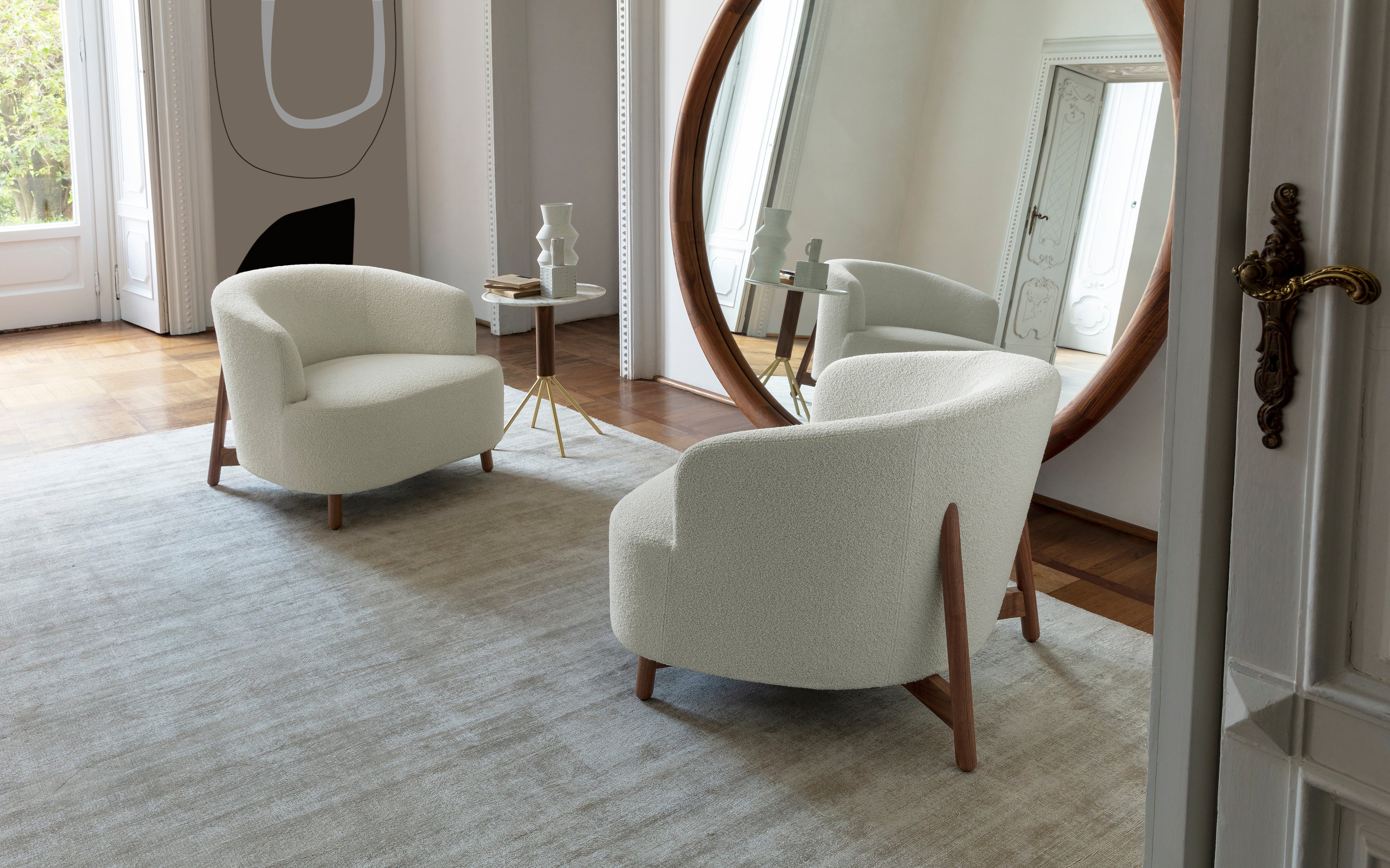 Modern living room with white armchairs, round mirror, and wooden floor.