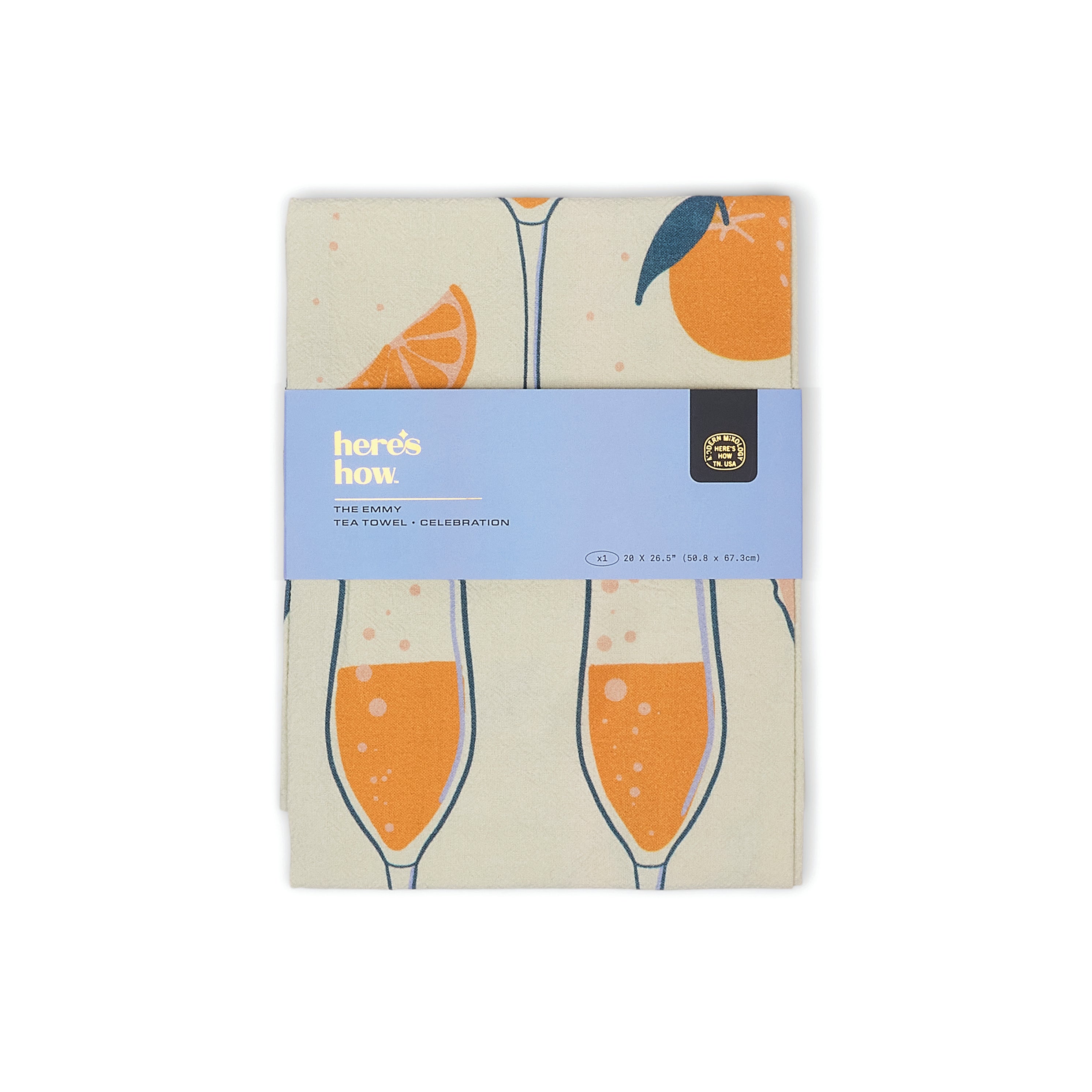 A folded tea towel with a champagne glass and citrus slice pattern, wrapped in a light blue paper band that reads 'here's how. tea towels - celebration'.