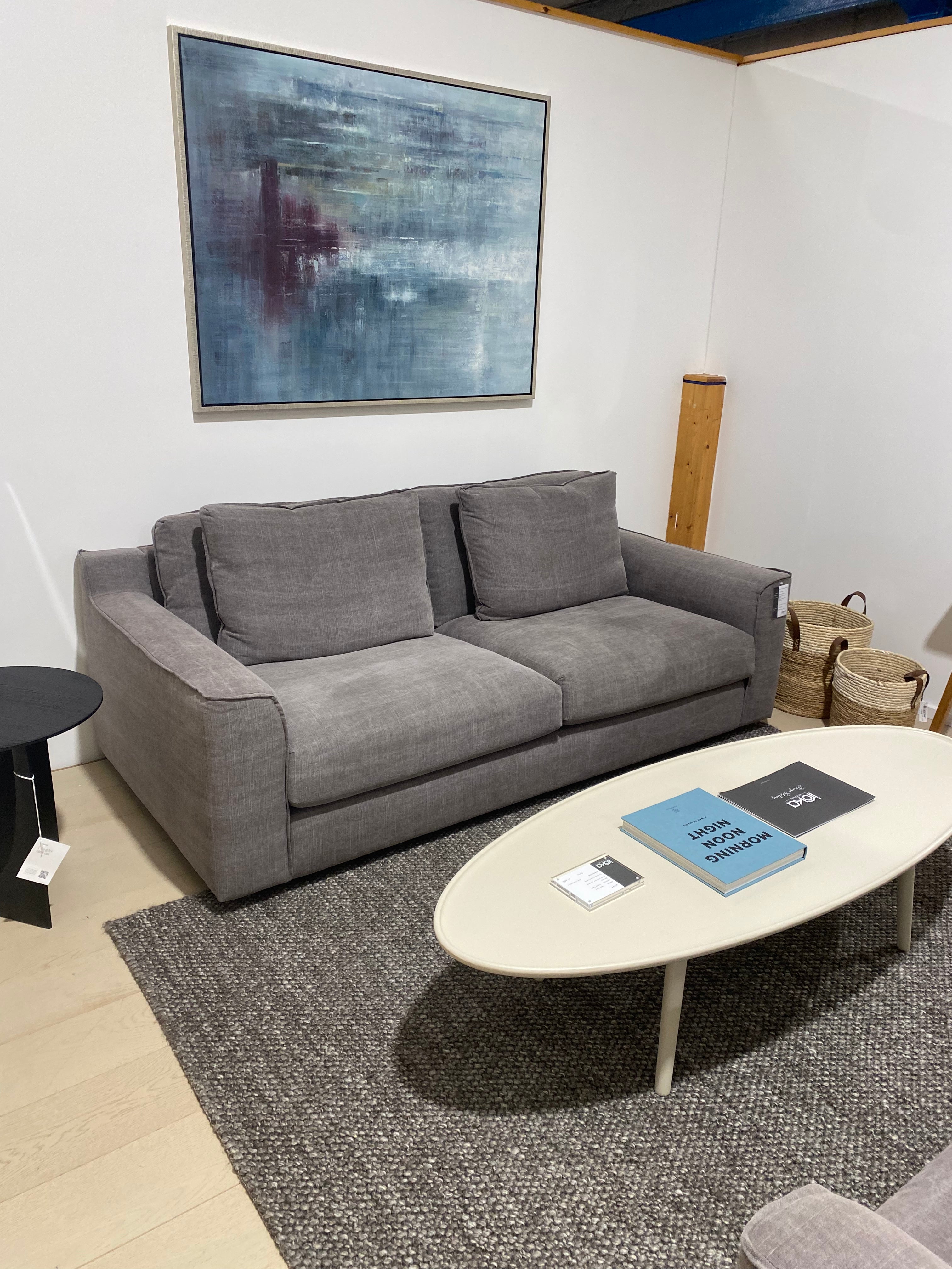 Gray sofa in a room with a round table and a painting on the wall.