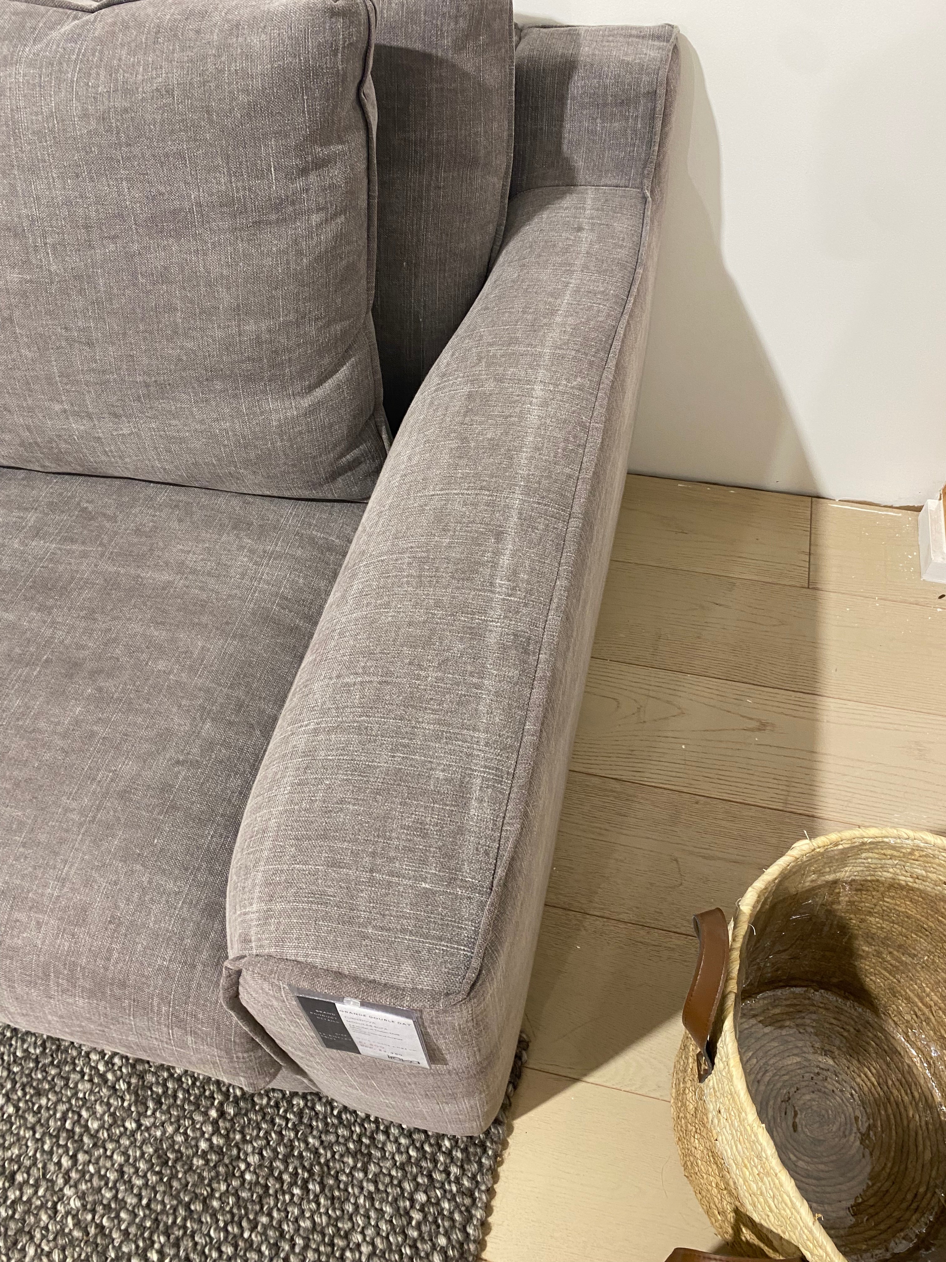 Gray sofa with a rolled-up cushion on a wooden floor.