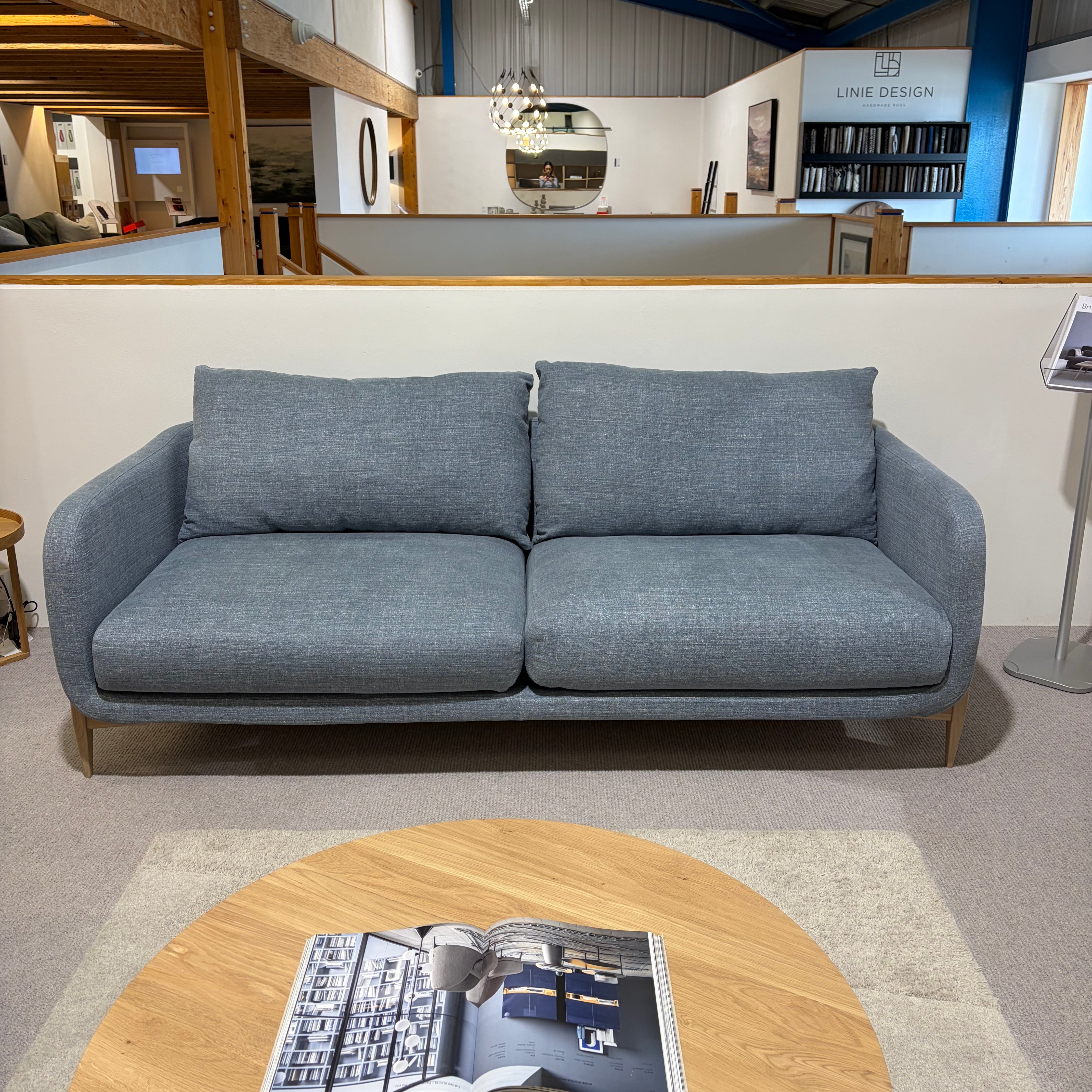 Gray sofa in a room with a round wooden table and a view of a kitchen.