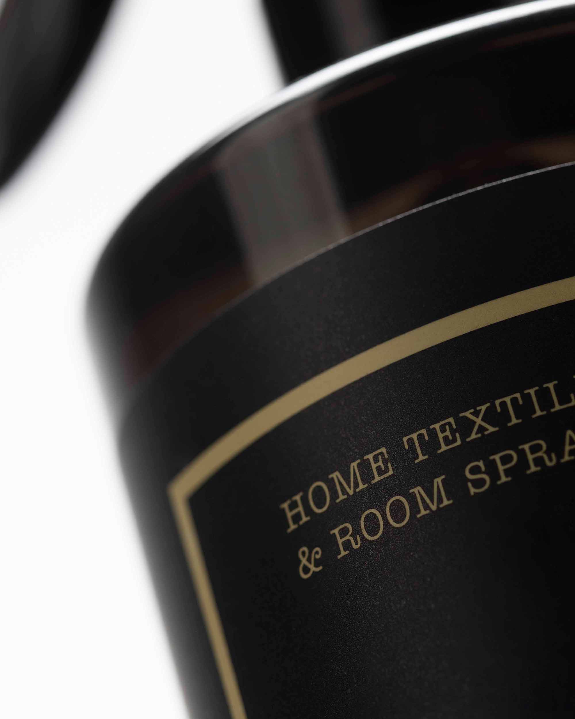 Close-up of a bottle with a label reading 'Home Textile & Room Spray' on a white background.