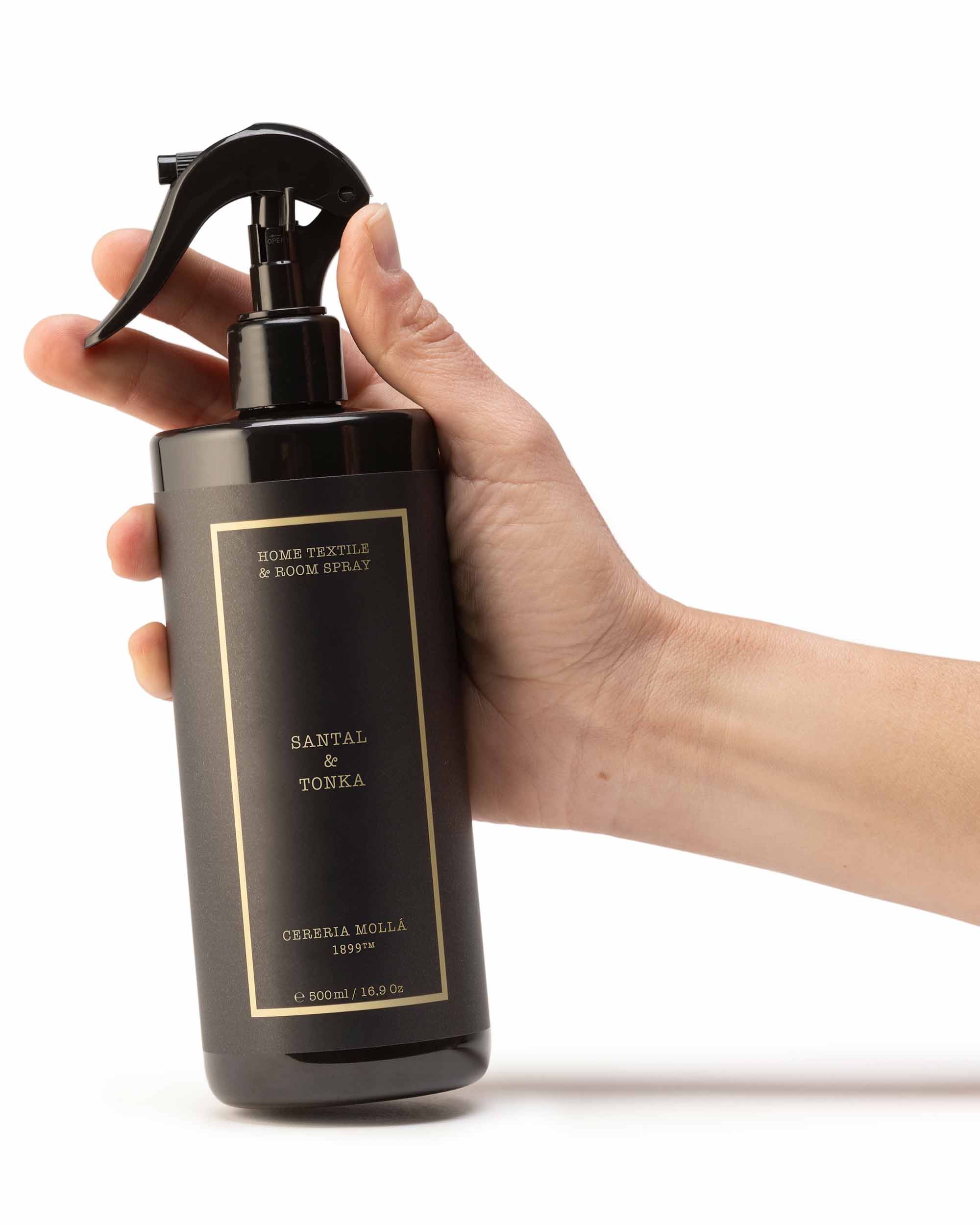 Hand holding a black spray bottle labeled 'Santal & Tonka' against a white background