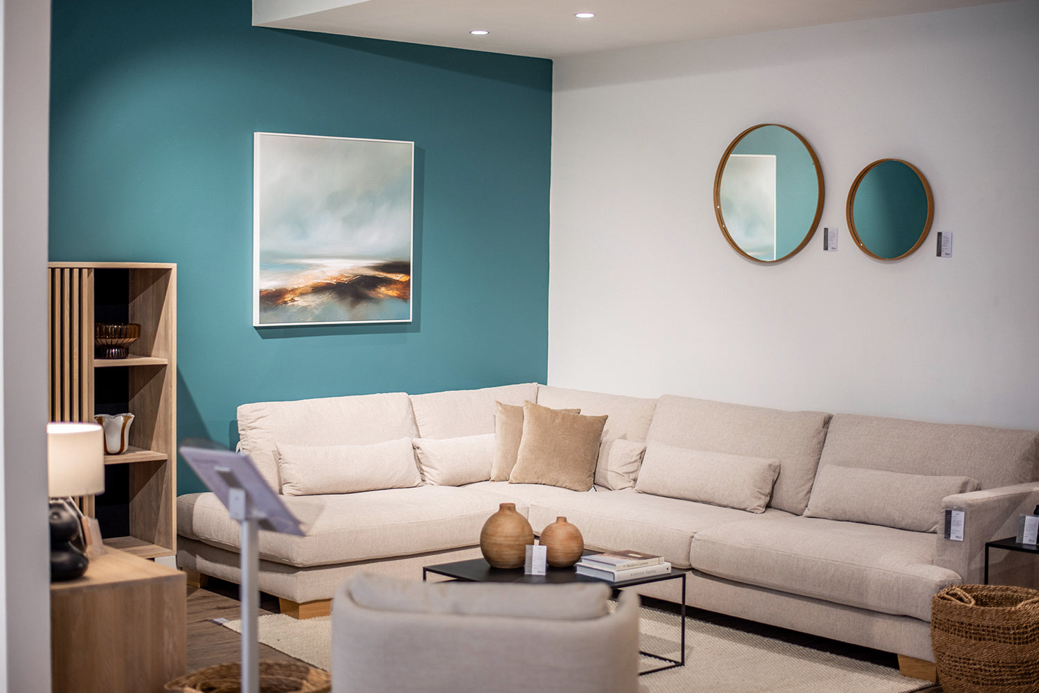 Furniture Showroom with bright teal feature wall room set with beige corner sofa and matching natural soft furnishings.