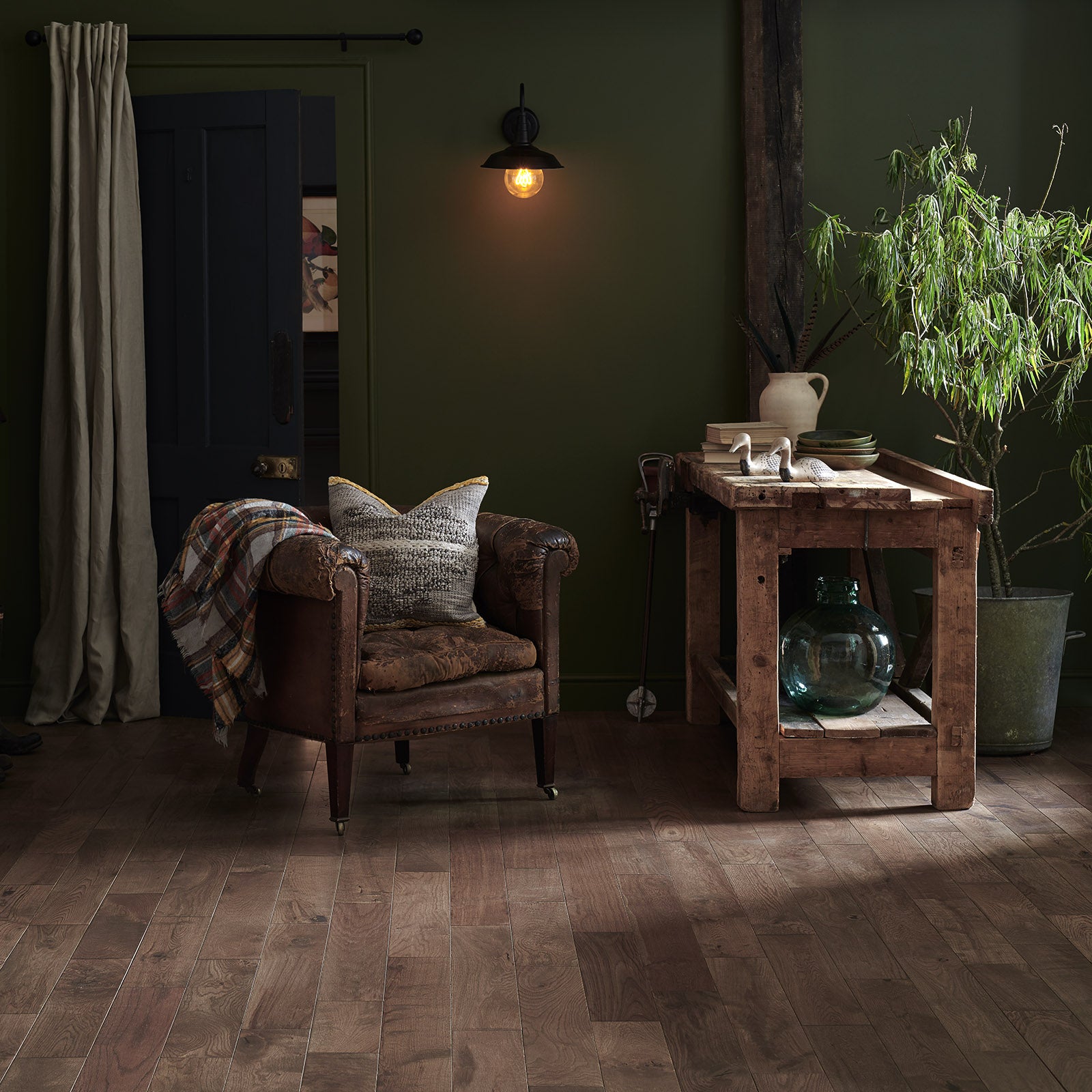 Cozy room with a wooden armchair, table, and decorative items against a dark green wall.