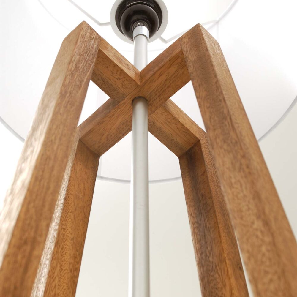 A close-up low-angle view of a wooden floor lamp light fixture, showing the warm brown wood frame and central silver metal rod against a white ceiling.